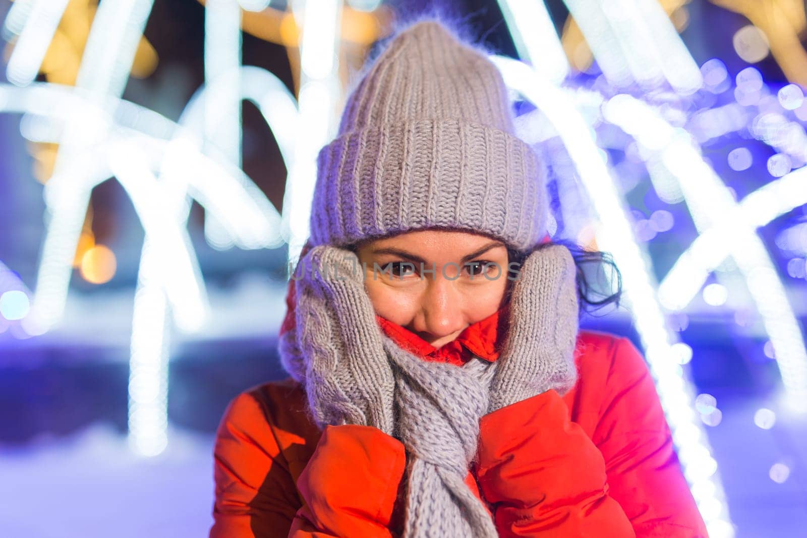 Happy funny young woman with winter clothes background evening city lights illumination. Christmas and winter holidays.