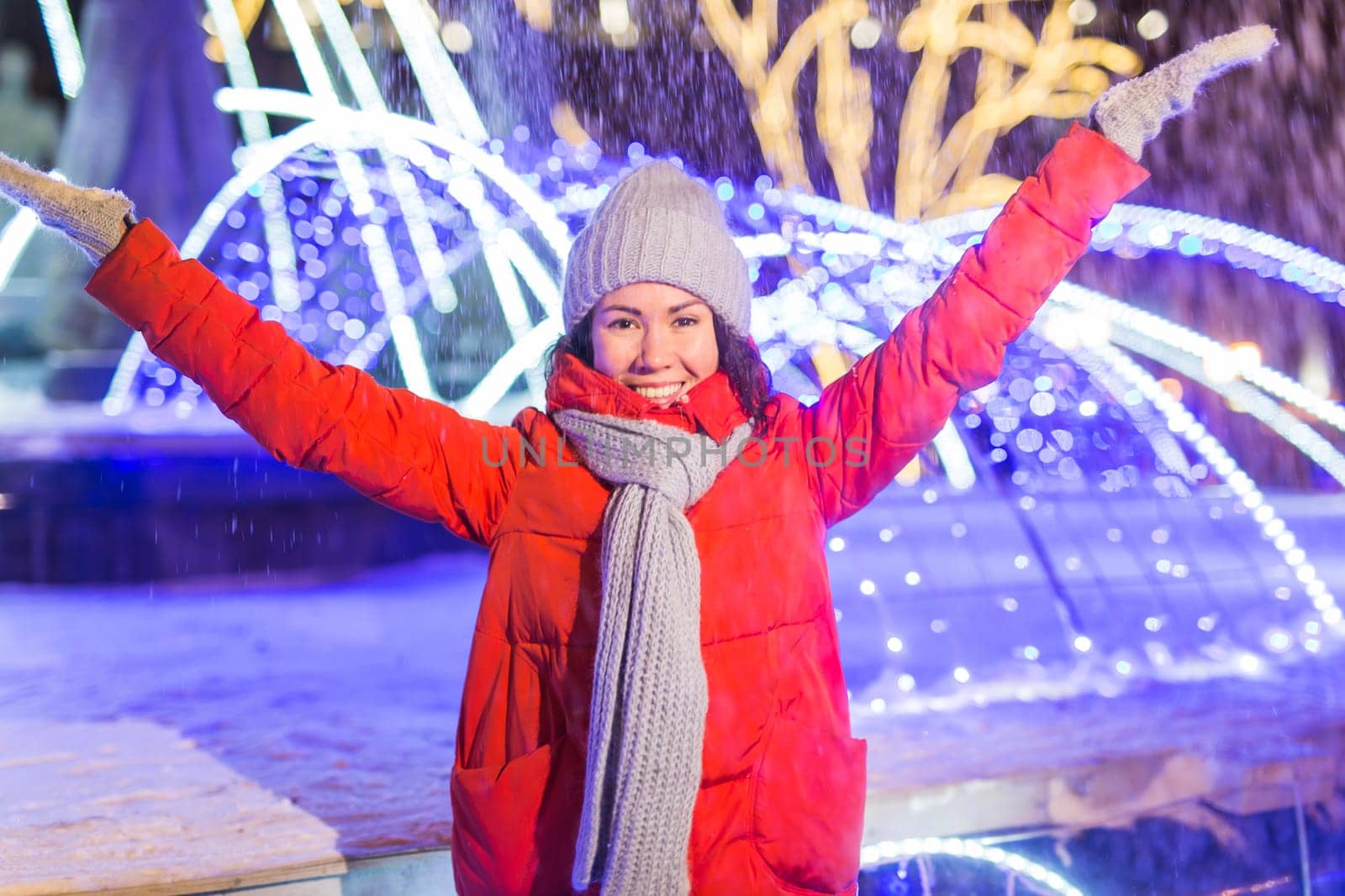 Girl having fun christmas decoration lights street. Young happy smiling woman wearing stylish knitted scarf and jacket outdoors. Model laughing. Winter wonderland city scene, New Year party.