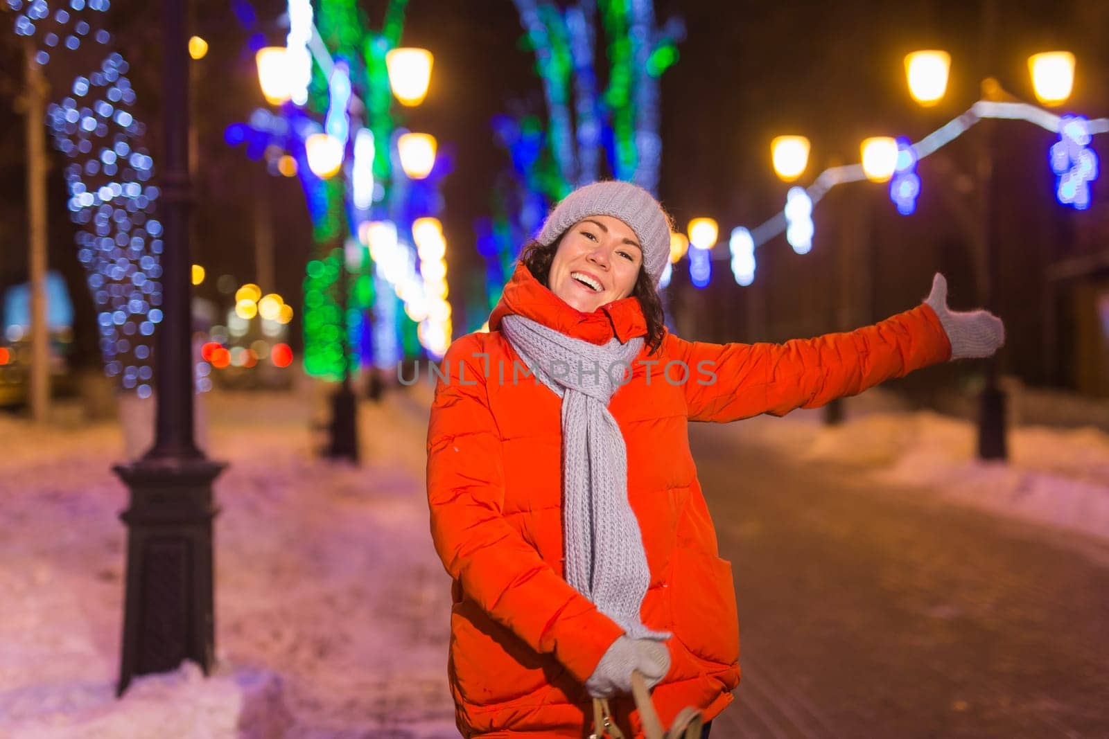 Happy funny young woman with winter clothes background evening city lights illumination. Christmas and winter holidays.