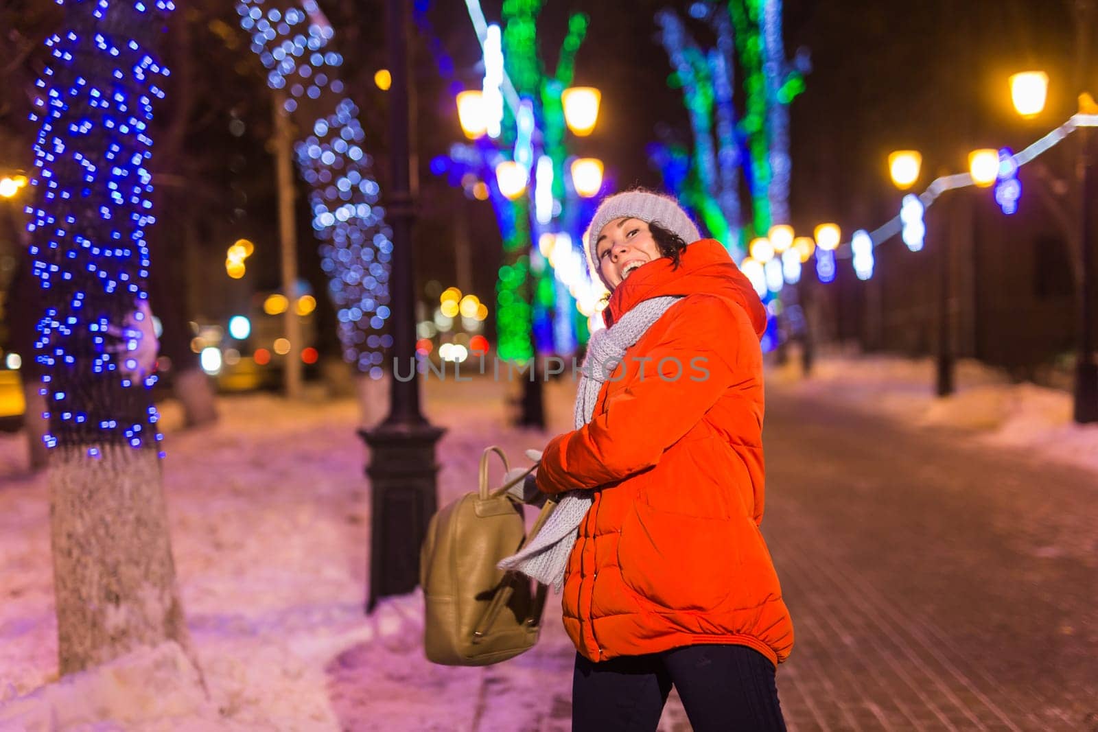 Winter holiday season. Christmas, New Year concept. Funny woman spend time having fun near illuminated and decorated showcase on city street.