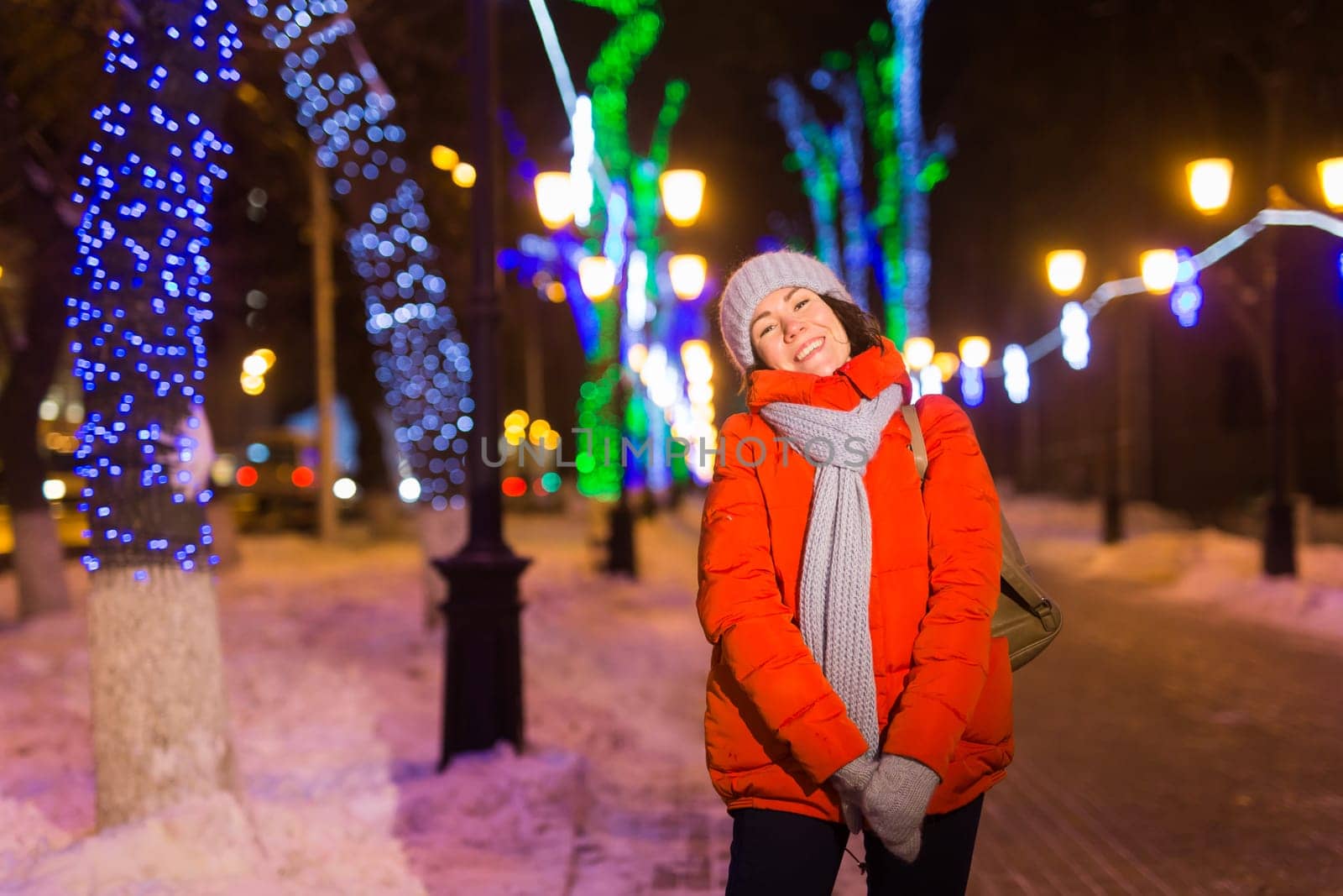 Happy funny young woman with winter clothes background evening city lights illumination. Christmas and winter holidays.