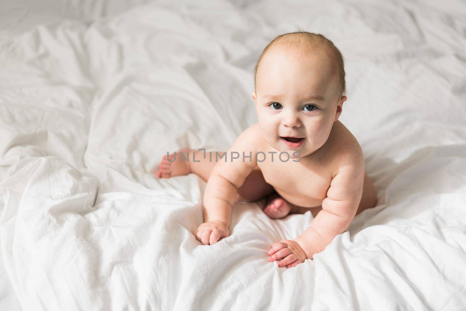 Adorable baby boy in white sunny bedroom. Newborn child relaxing in bed. Nursery for young children. Textile and bedding for kids. Family morning at home