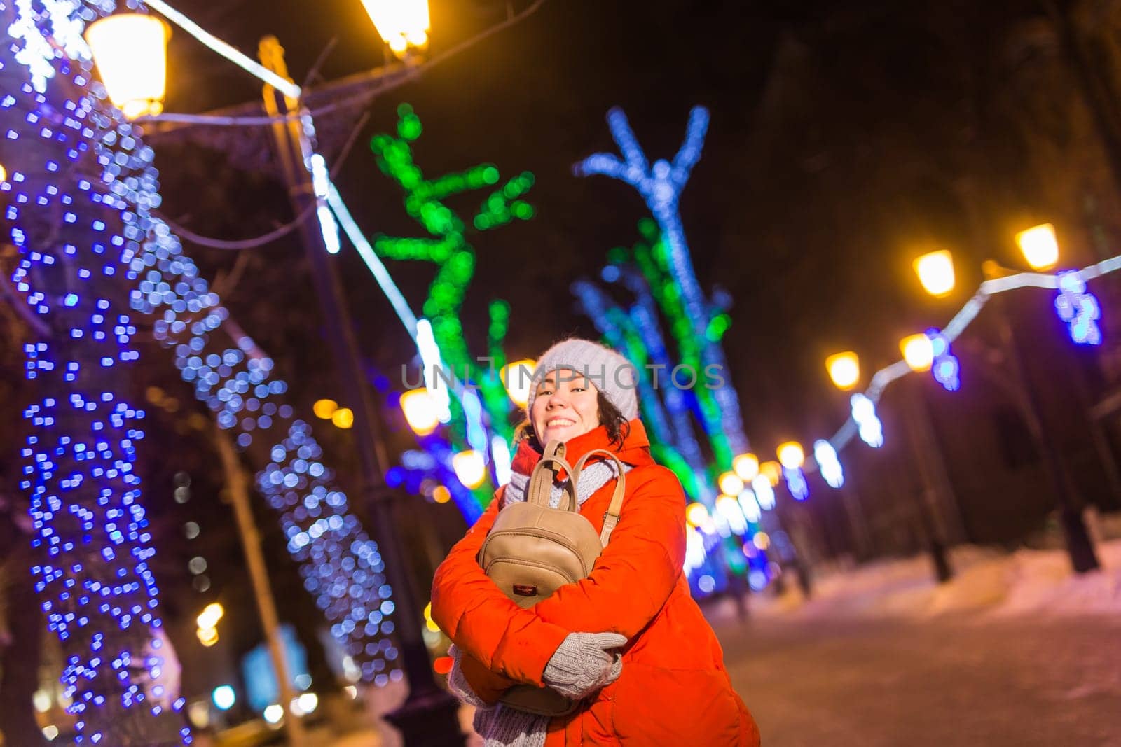 Happy funny young woman with winter clothes background evening city lights illumination. Christmas and winter holidays.