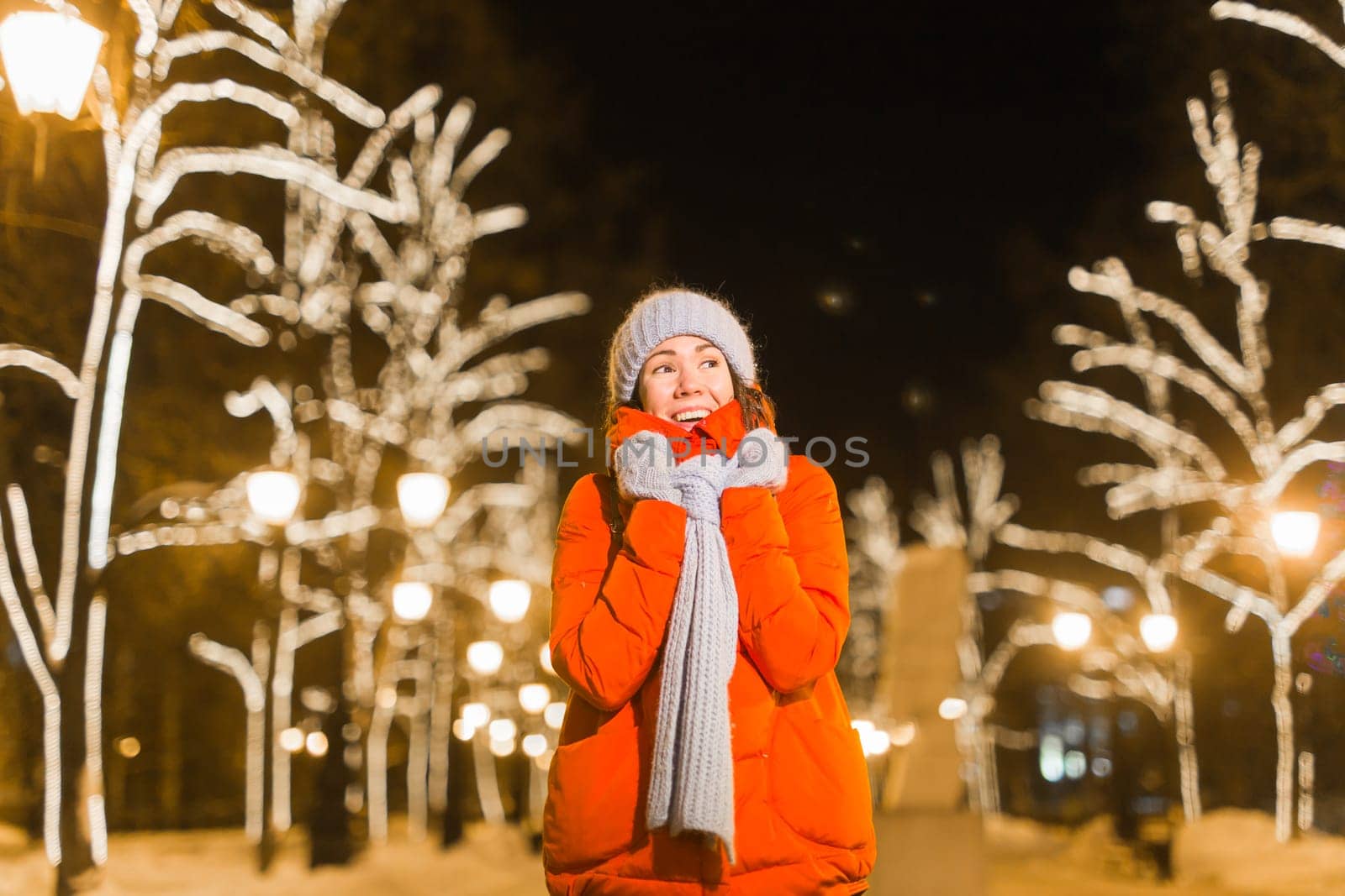 Winter holiday season. Christmas, New Year concept. Funny woman spend time having fun near illuminated and decorated showcase on city street.