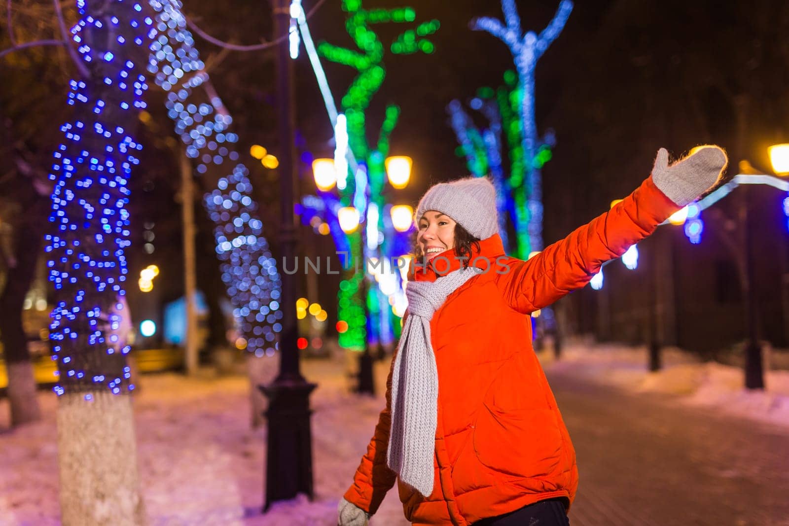 Happy funny young woman with winter clothes background evening city lights illumination. Christmas and winter holidays.