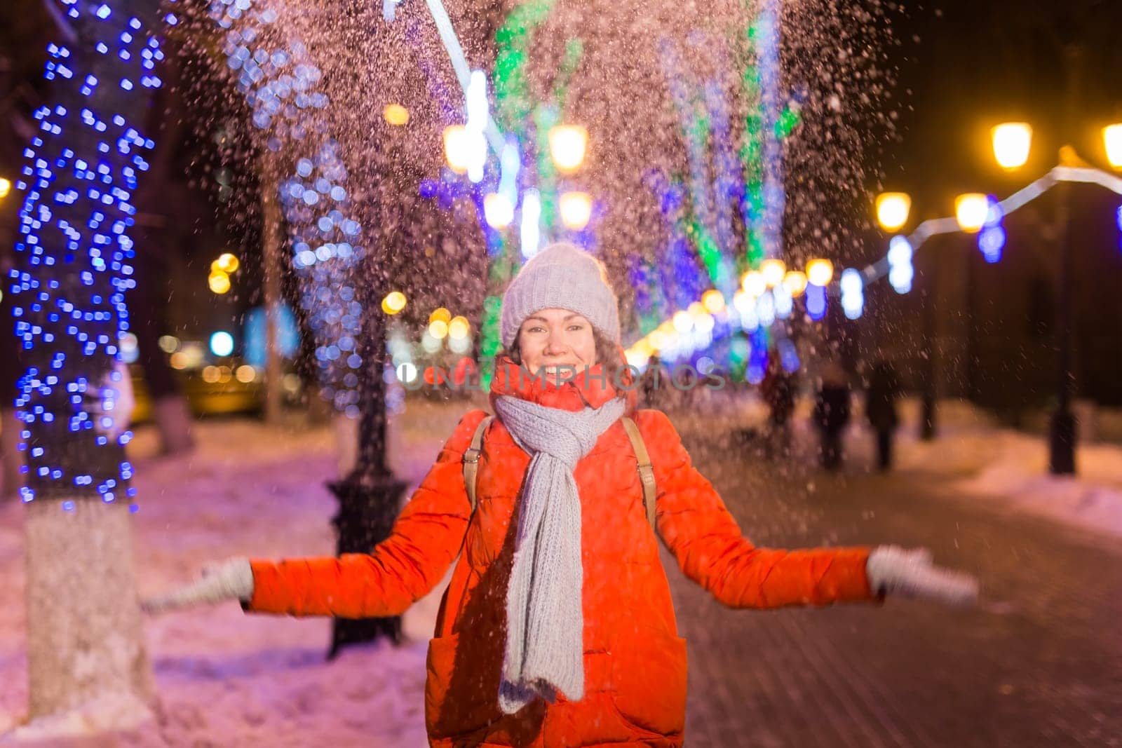 Happy funny young woman with winter clothes background evening city lights illumination. Christmas and winter holidays.