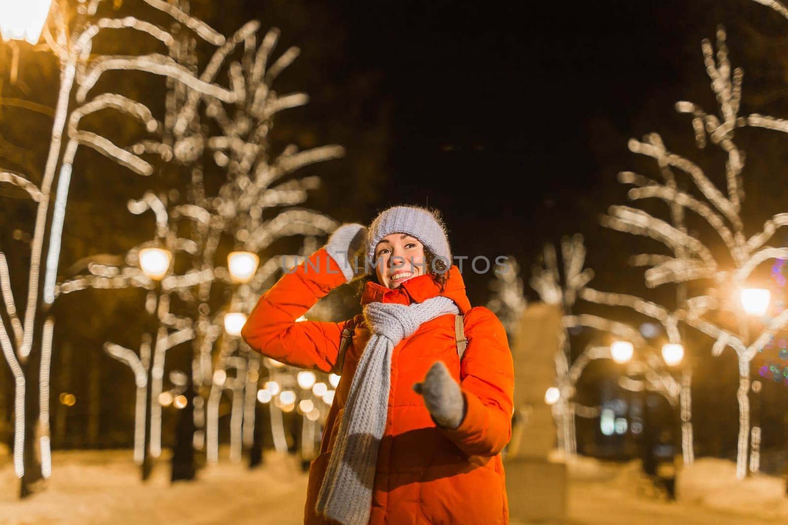 Girl having fun christmas decoration lights street. Young happy smiling woman wearing stylish knitted scarf and jacket outdoors. Model laughing. Winter wonderland city scene, New Year party.