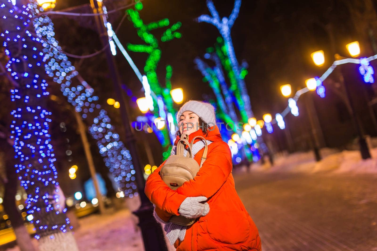 Winter holiday season. Christmas, New Year concept. Funny woman spend time having fun near illuminated and decorated showcase on city street.