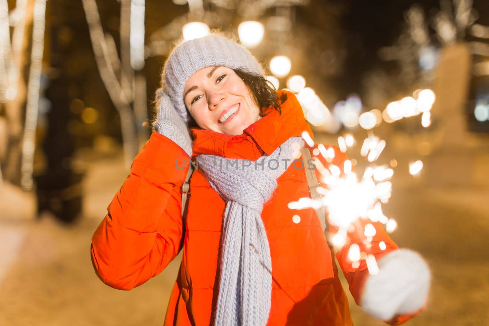 Girl holding a sparkler in her hand. Outdoor winter city background, snow, snowflakes