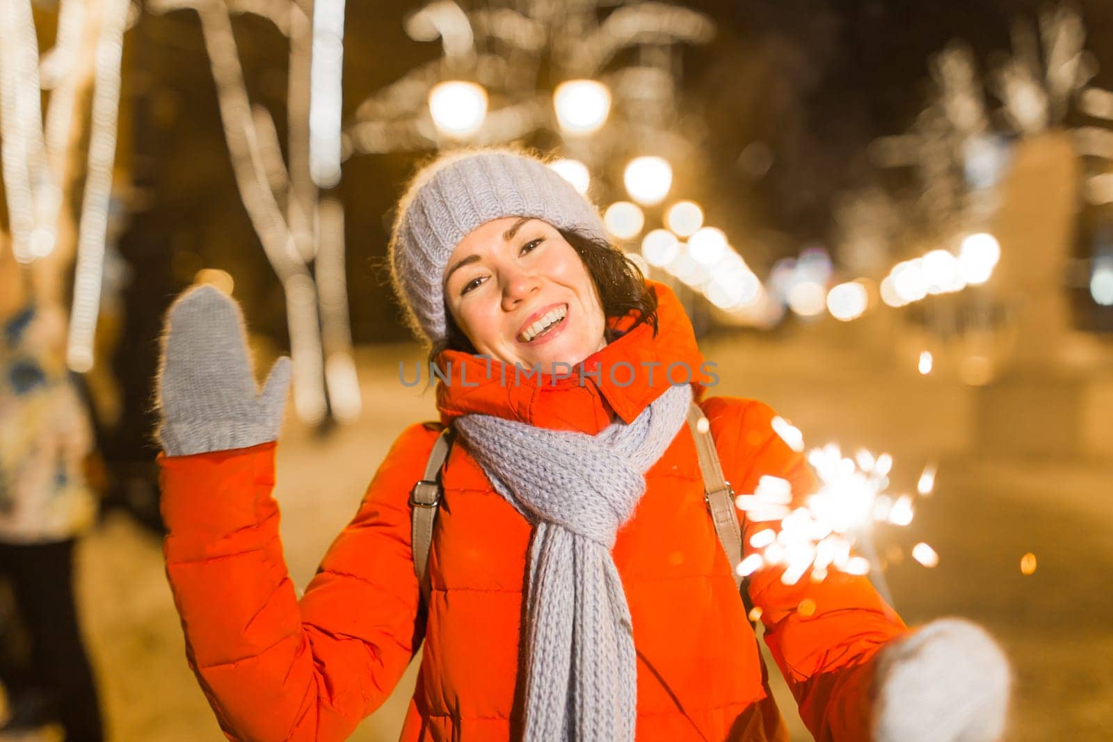 Girl holding a sparkler in her hand. Outdoor winter city background, snow, snowflakes