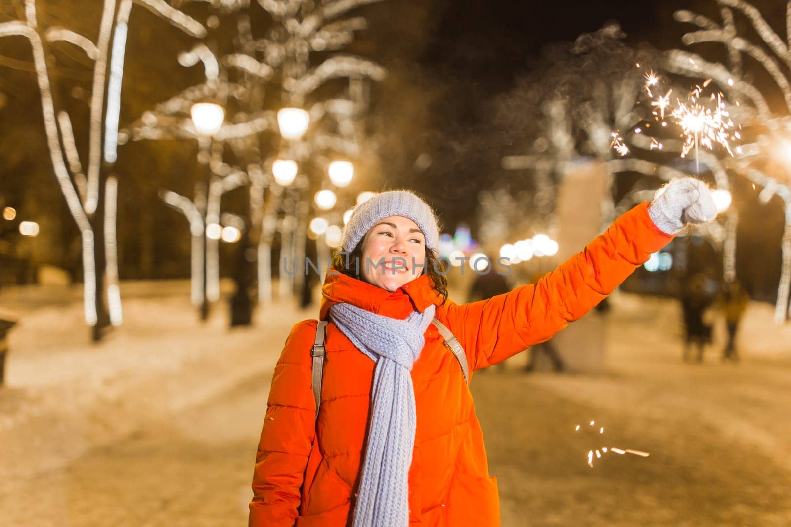 Girl holding a sparkler in her hand. Outdoor winter city background, snow, snowflakes