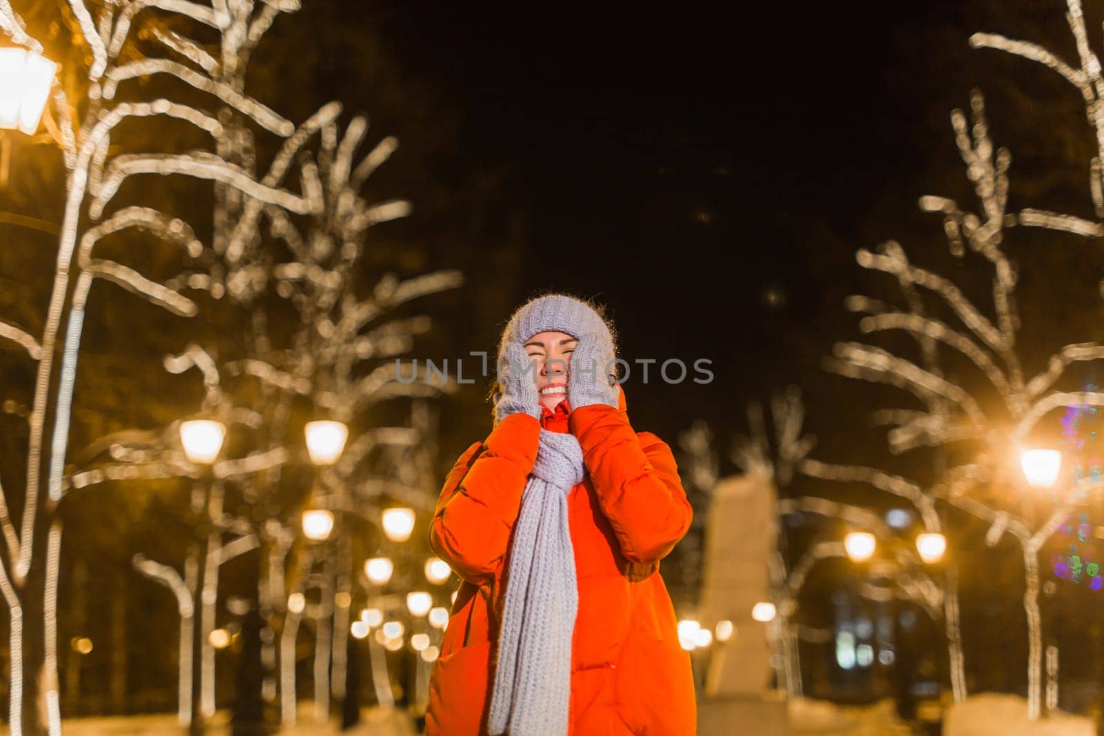 Happy funny young woman with winter clothes background evening city lights illumination. Christmas and winter holidays.