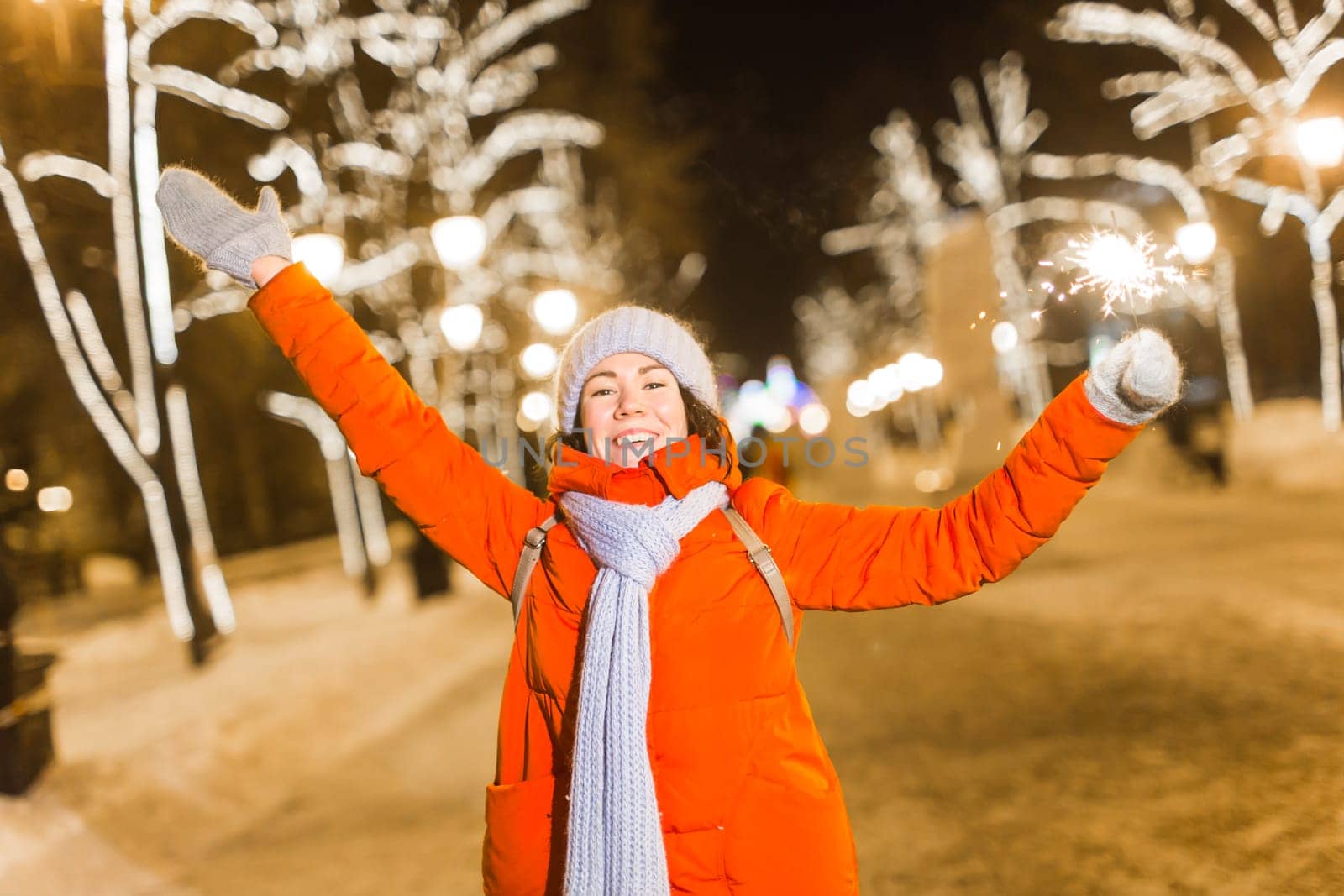 Girl holding a sparkler in her hand. Outdoor winter city background, snow, snowflakes