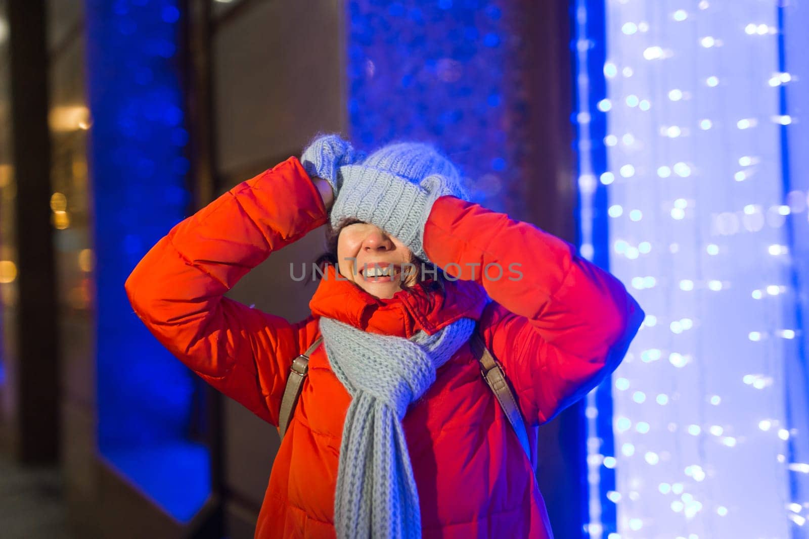 Happy funny young woman with winter clothes background evening city lights illumination. Christmas and winter holidays.