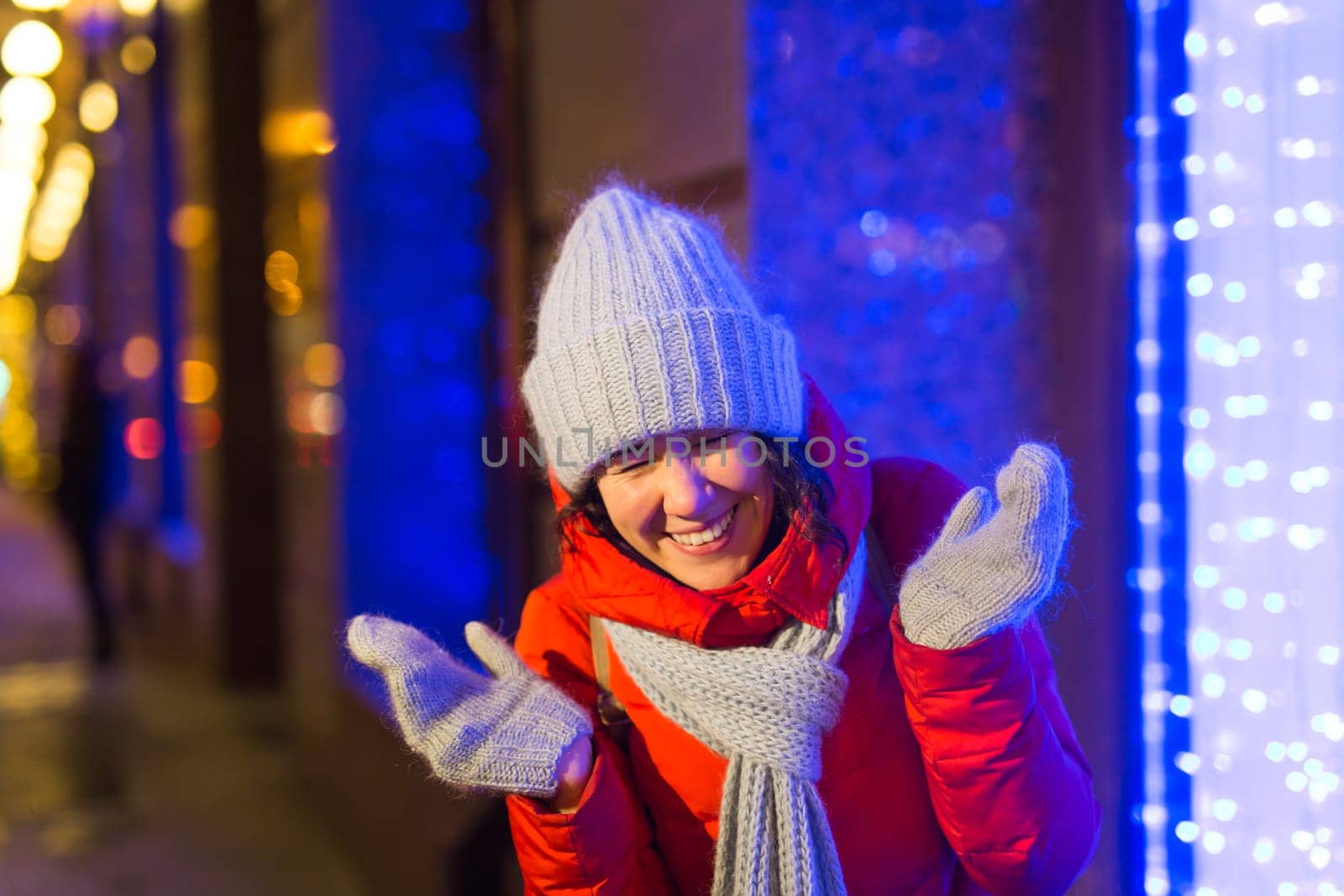 Girl having fun christmas decoration lights street. Young happy smiling woman wearing stylish knitted scarf and jacket outdoors. Model laughing. Winter wonderland city scene, New Year party.