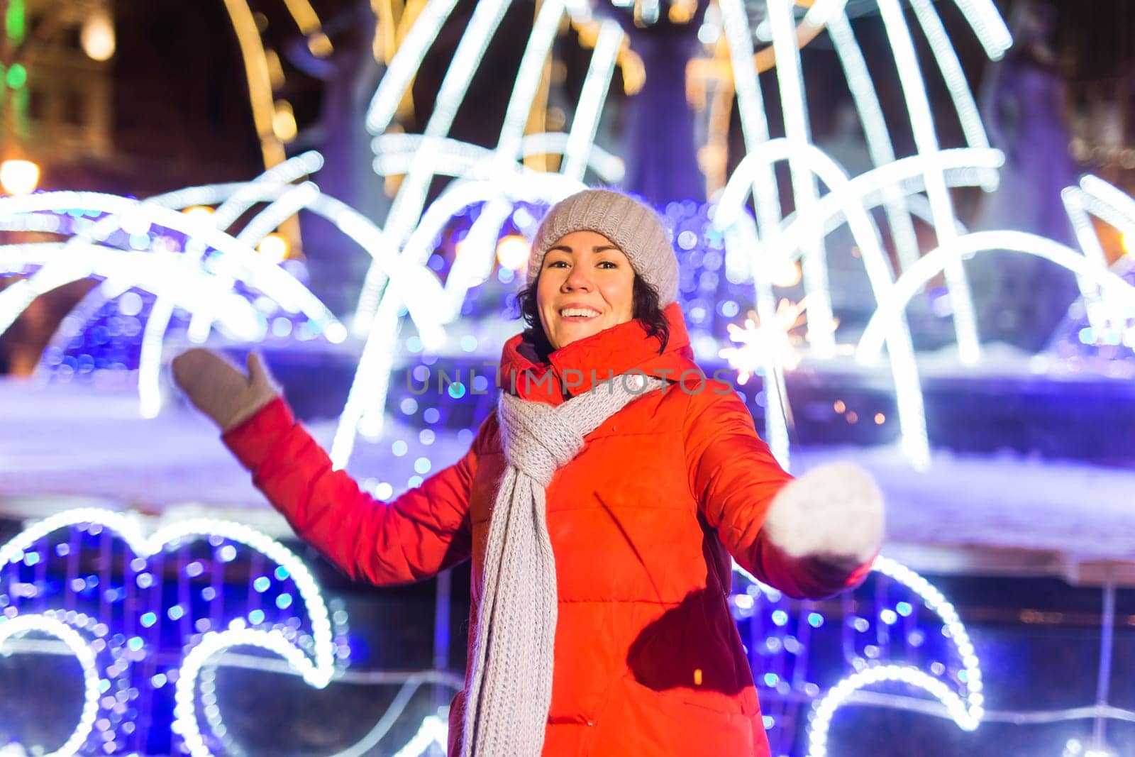 Girl holding a sparkler in her hand. Outdoor winter city background, snow, snowflakes