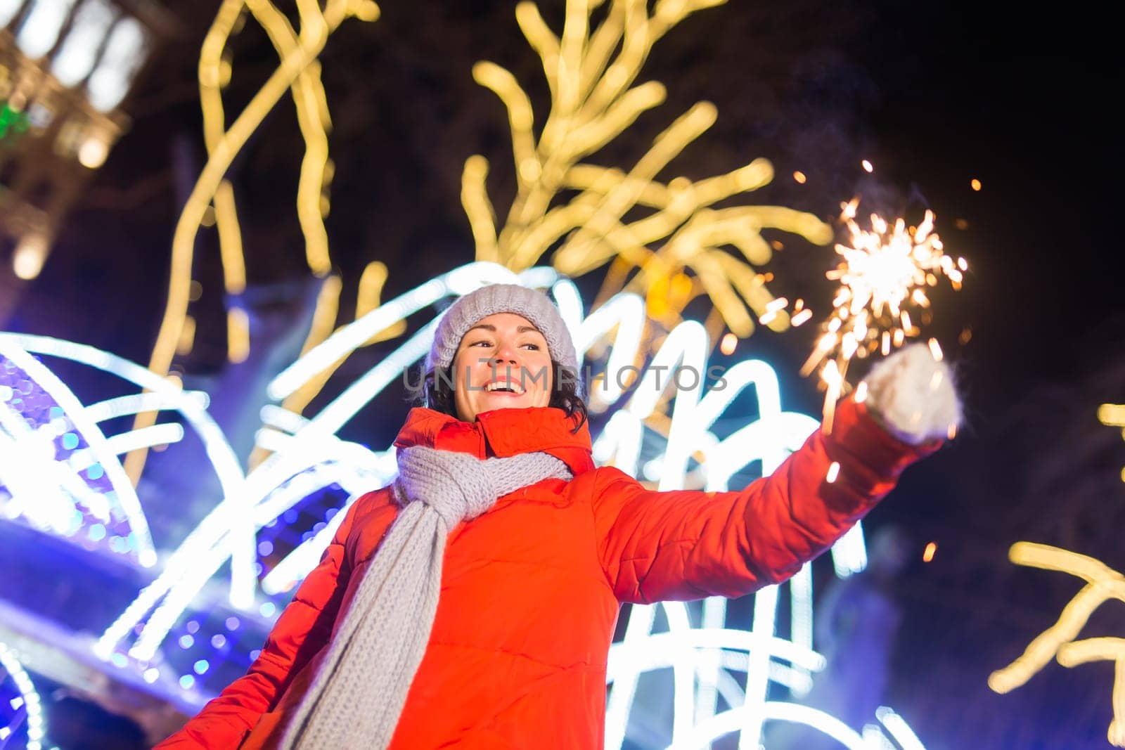 Young beautiful woman in knitted hat and scarf standing in the city with bengal light, sparkler. Concept celebration and christmas