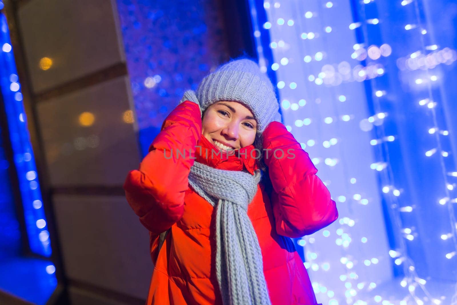 Winter holiday season. Christmas, New Year concept. Funny woman spend time having fun near illuminated and decorated showcase on city street.