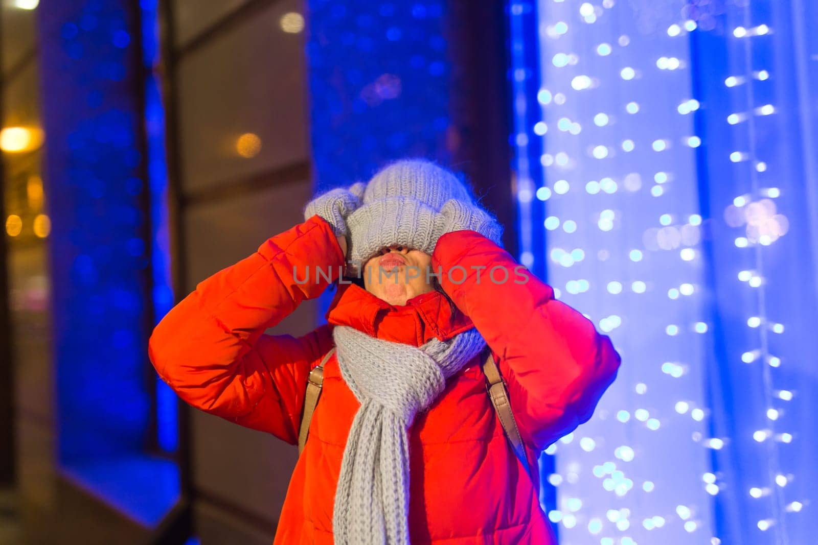 Happy funny young woman with winter clothes background evening city lights illumination. Christmas and winter holidays.