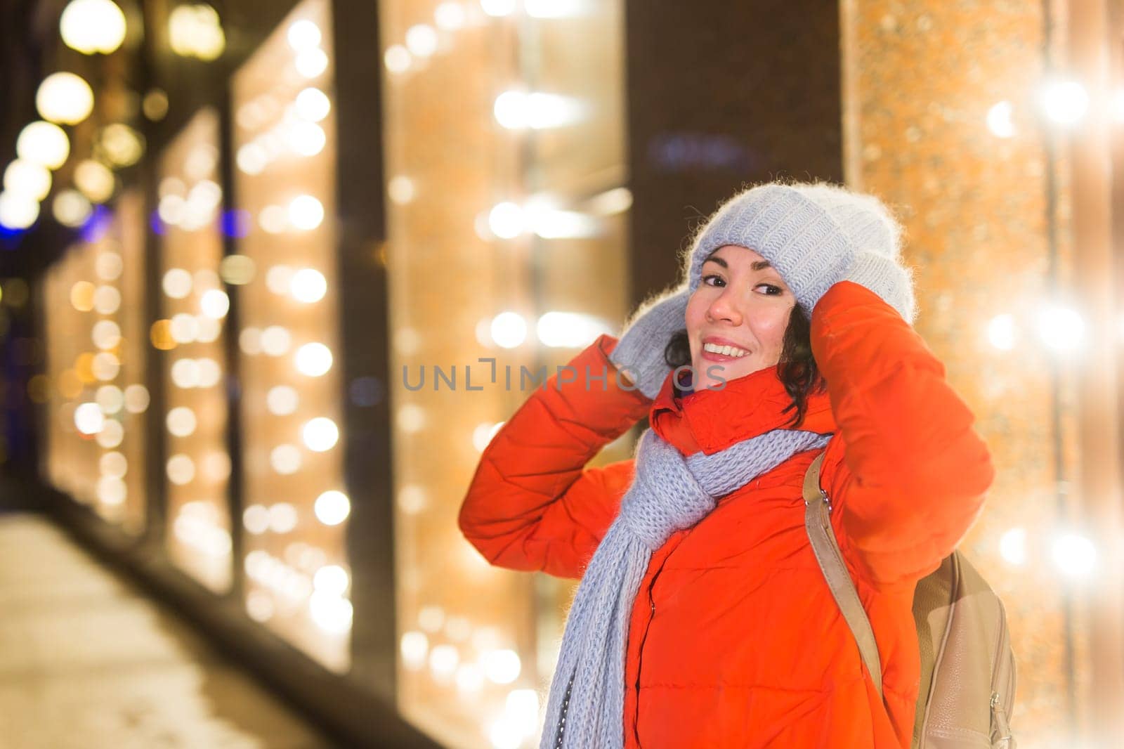 Girl having fun christmas decoration lights street. Young happy smiling woman wearing stylish knitted scarf and jacket outdoors. Model laughing. Winter wonderland city scene, New Year party.