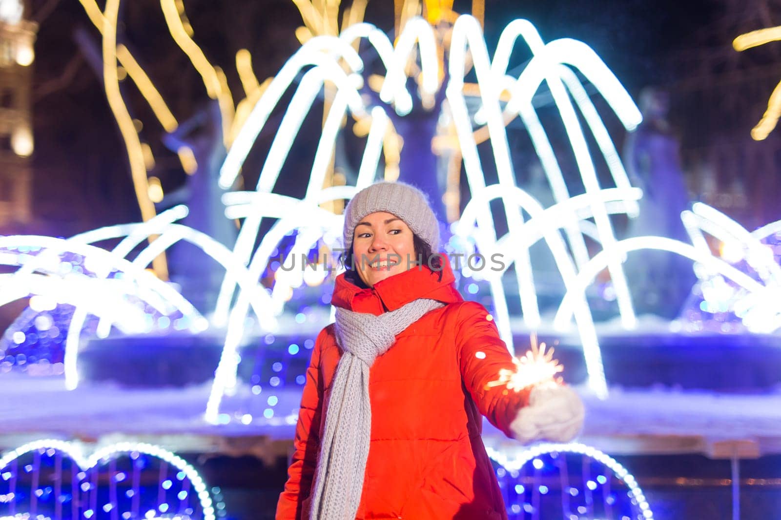 Girl holding a sparkler in her hand. Outdoor winter city background, snow, snowflakes