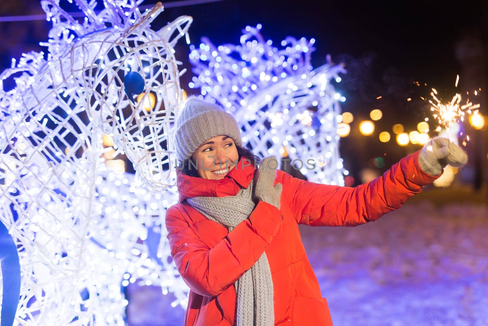 Girl holding a sparkler in her hand. Outdoor winter city background, snow, snowflakes