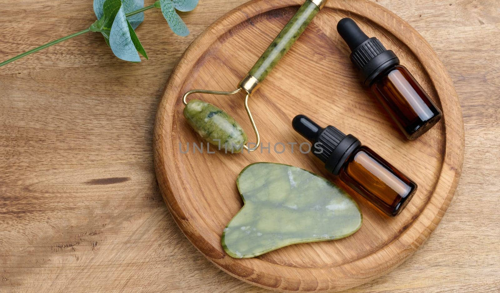 Brown glass bottle with a pipette,  stone hand massager for cosmetic procedures on a wooden background, top view
