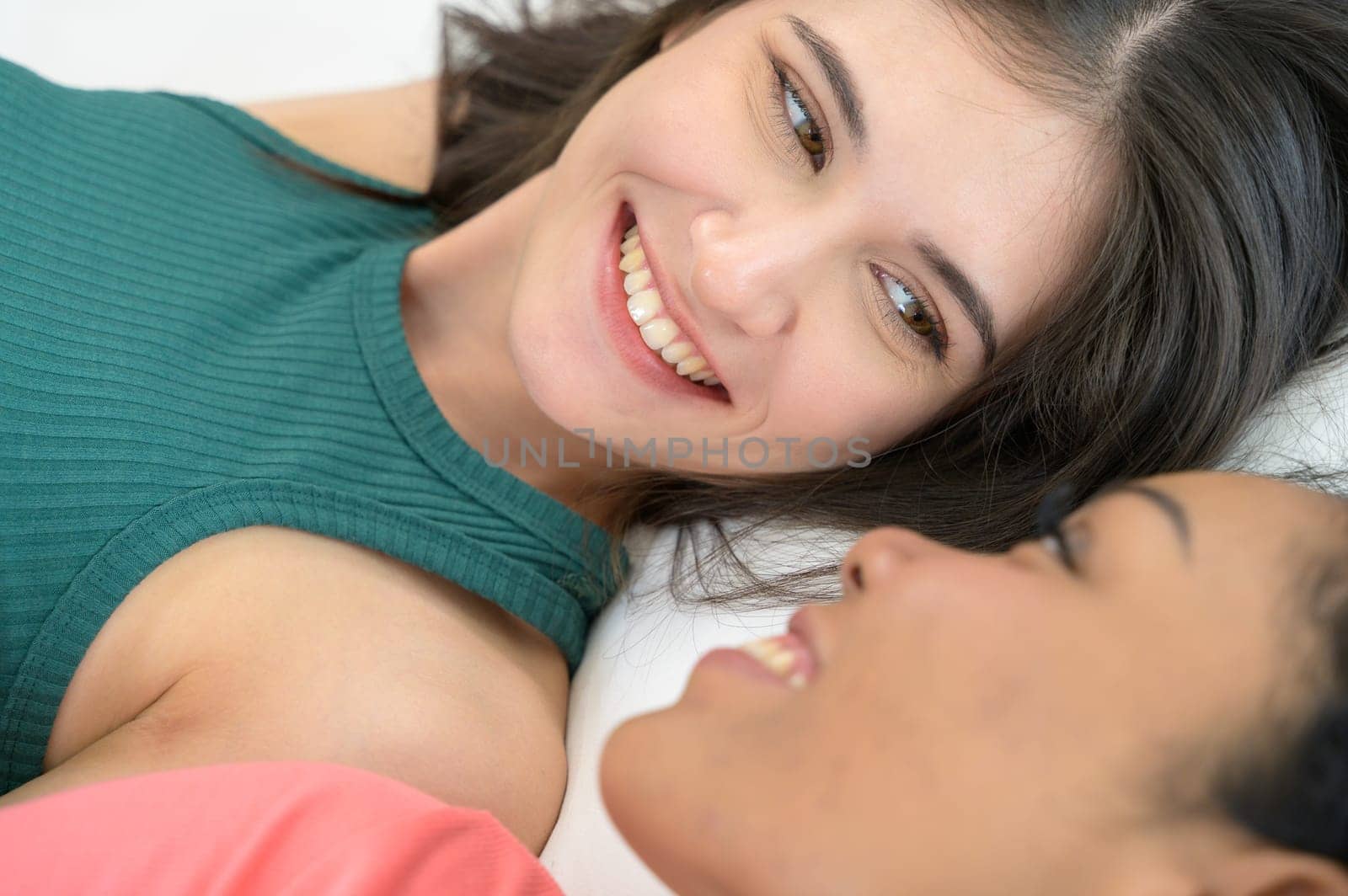 Close up of happy young couple lying in bed together. Lesbian multiethnic couple enjoying the company of each other at home.