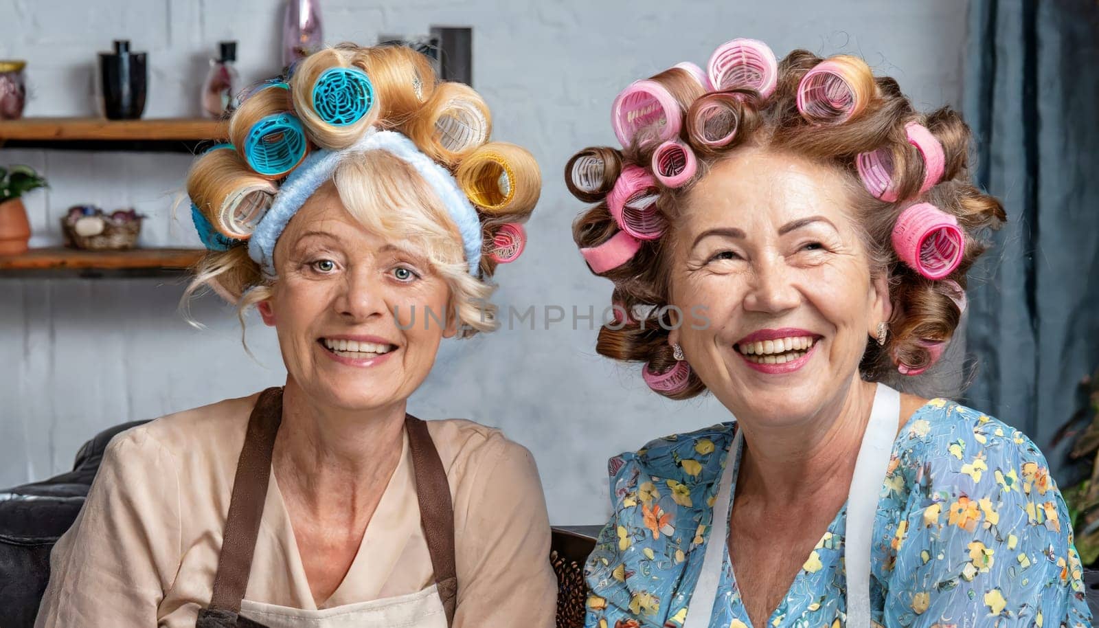Two older ladies having fun at the hairdresser. They have colorful curlers in their hair.