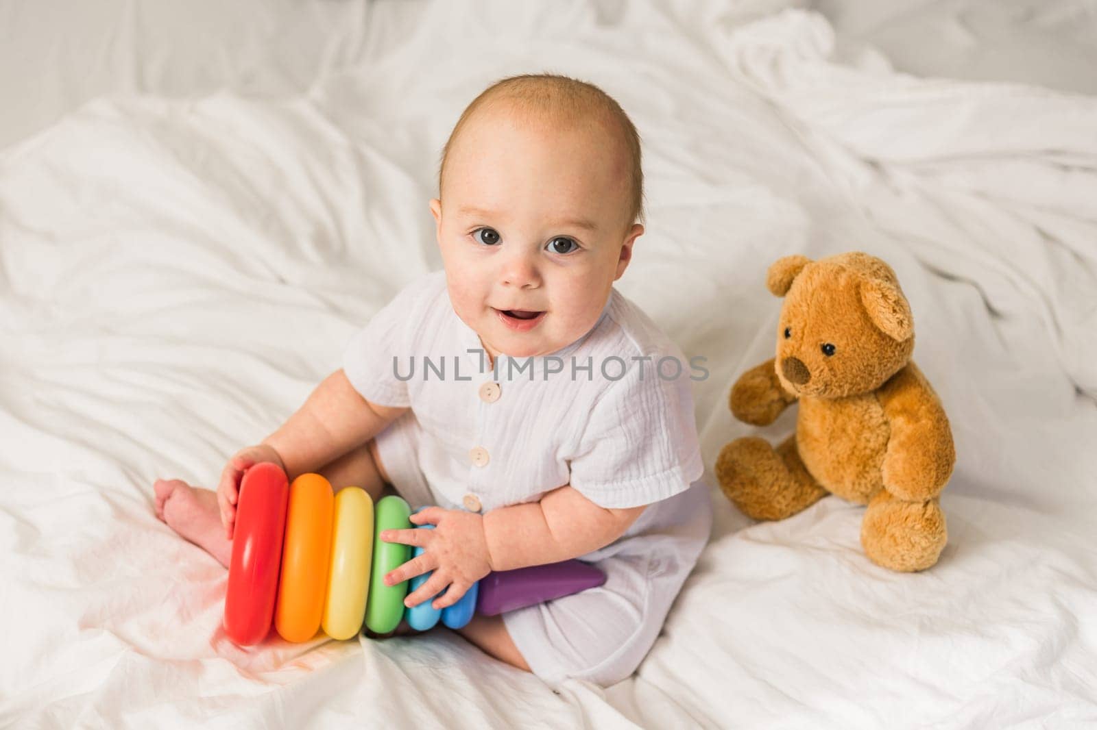Baby boy in white bedroom. Newborn child in bed with toys. Nursery for children. Textile, pillows and bedding for kids. Family morning at home. New born kid time with toy bear