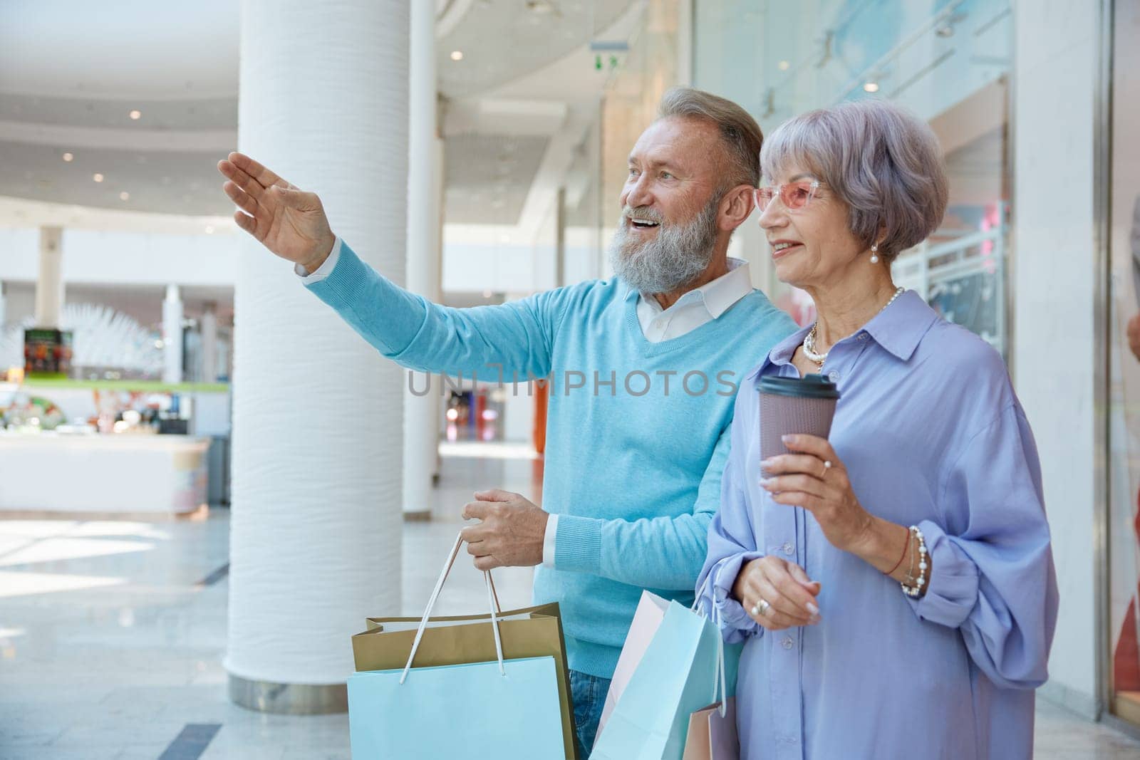 Happy elderly couple in shopping mall going for Black Friday sales. Happy retirement, price clearance and discounts concept