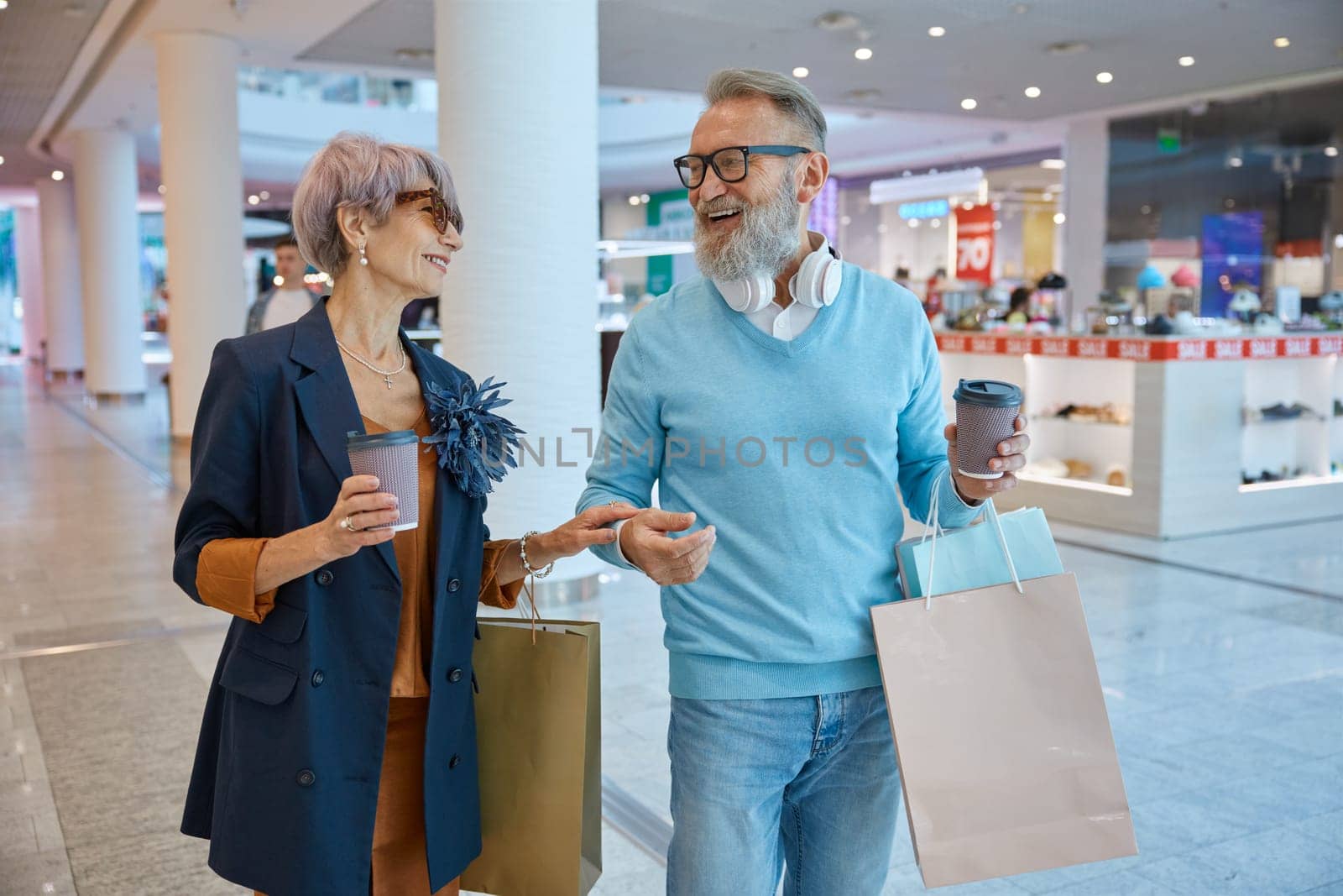 Fashionable elderly couple enjoying shopping tour on black friday weekends. Happy aged man and woman on retirement choosing new trendy outfit in city mall