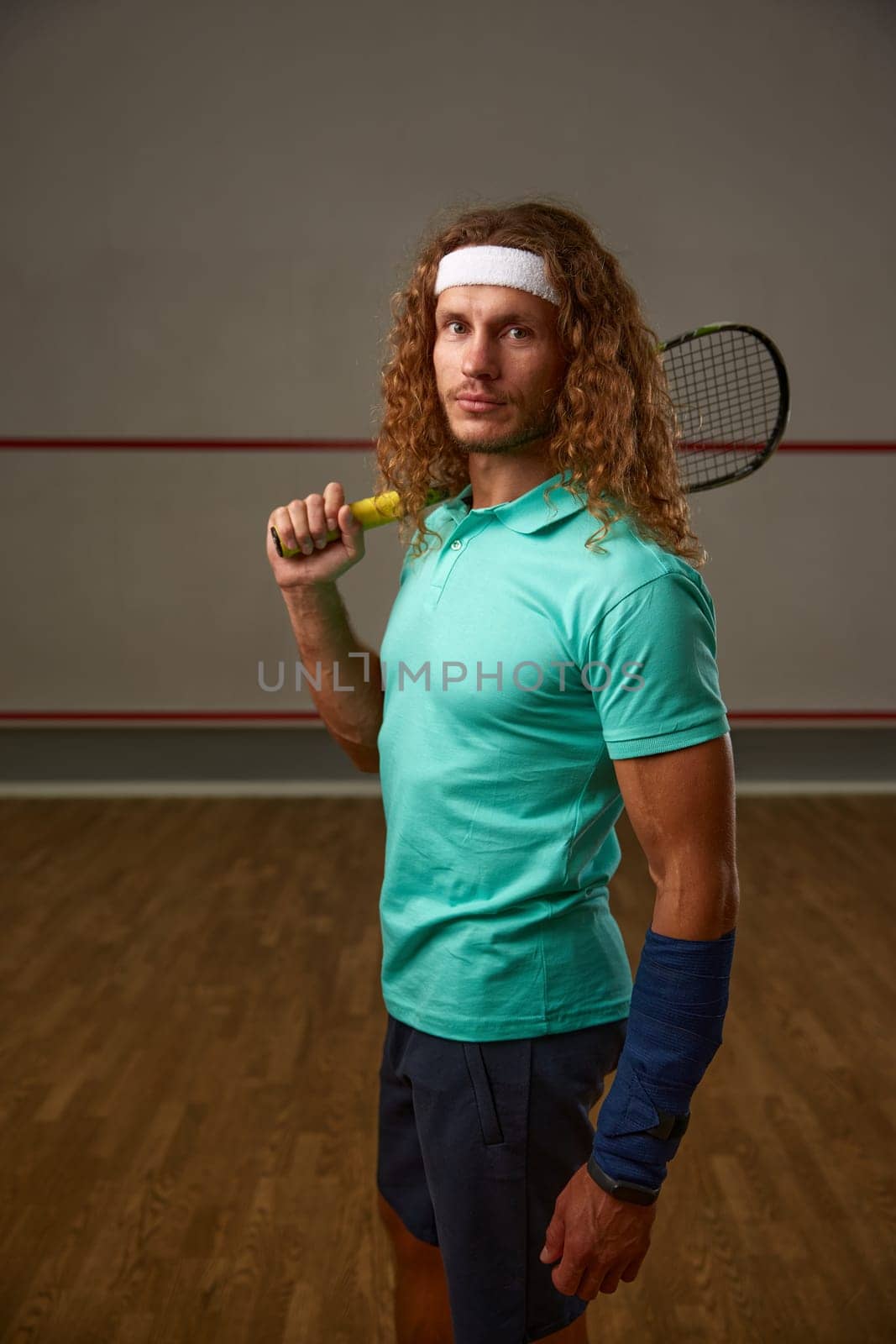 Portrait of male squash player standing with racket ready for game looking confidently at camera