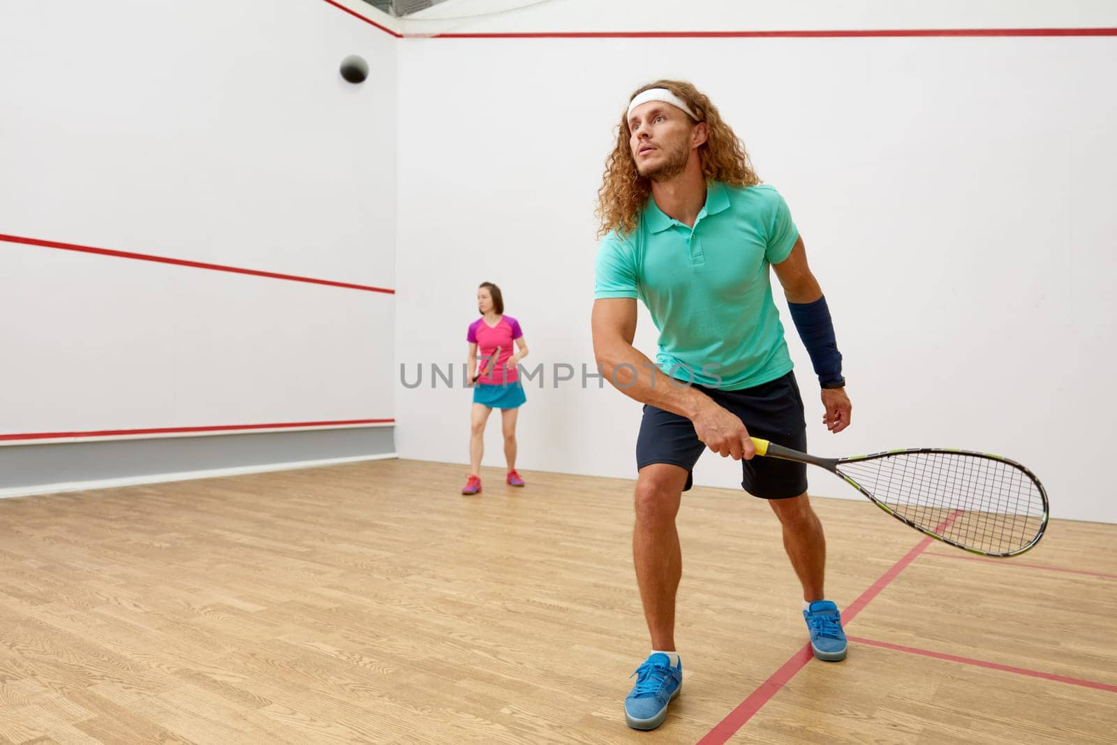 Squash male player with racket playing game with female friend at indoor training court