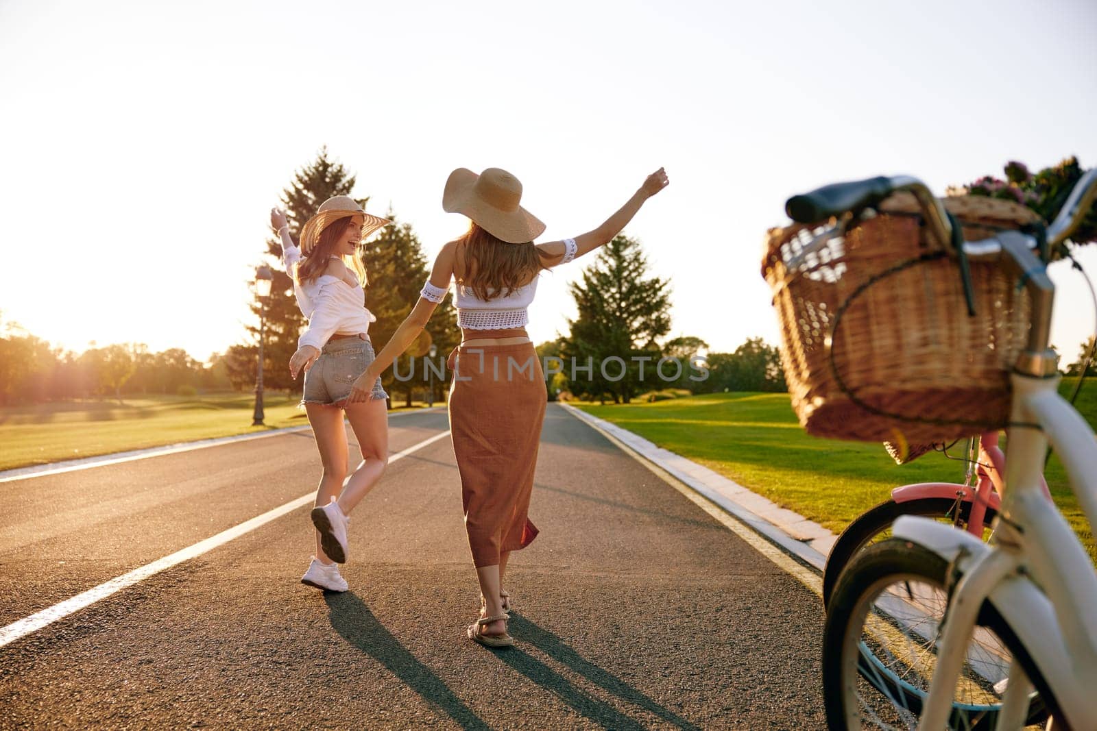 Young female friends enjoying road trip on bicycle spending weekend together. View on excited joyful teenager girls running on road and bike parked at sidewalk