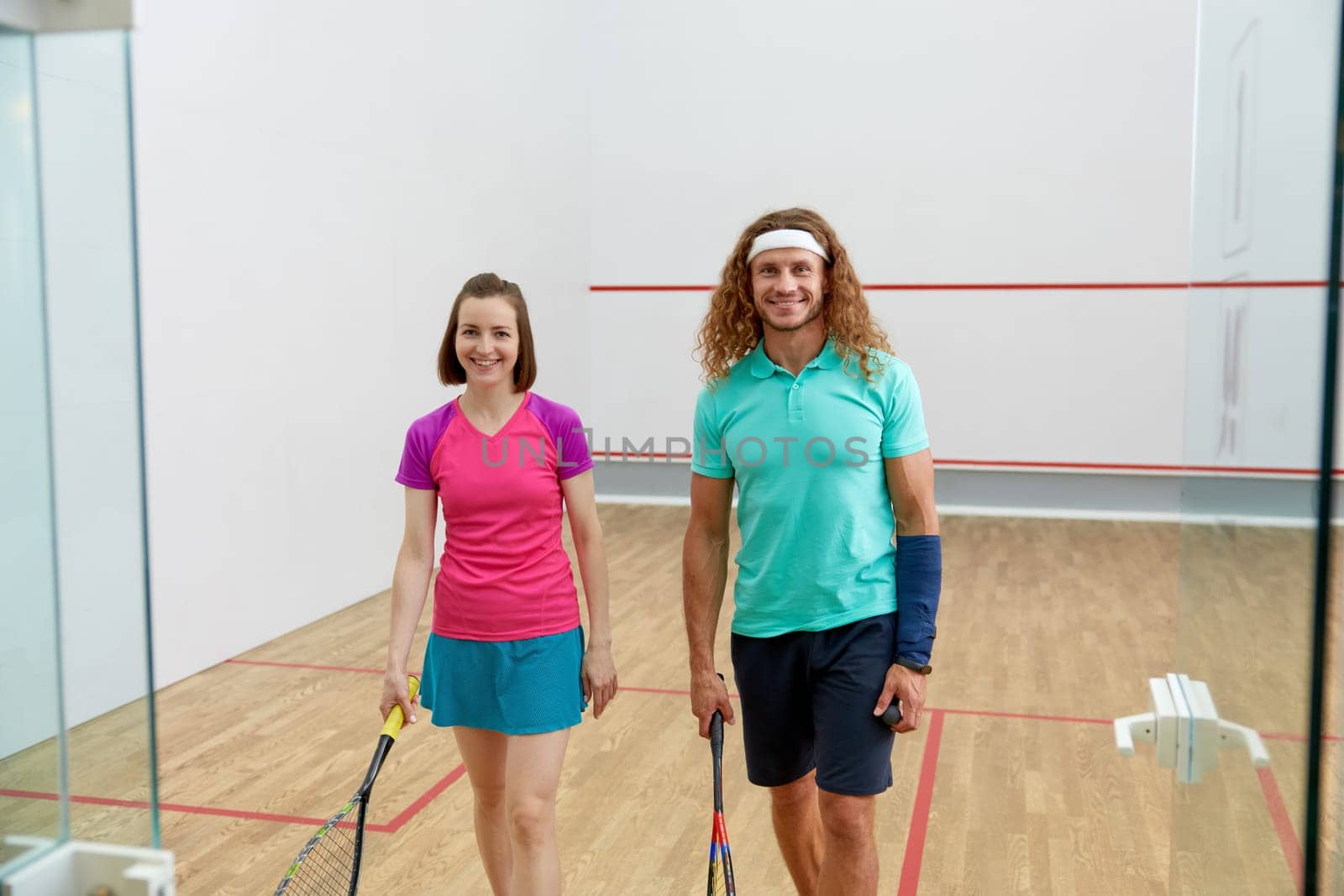 Satisfied man and woman athlete after successful squash game. View from glass sportive club doorway