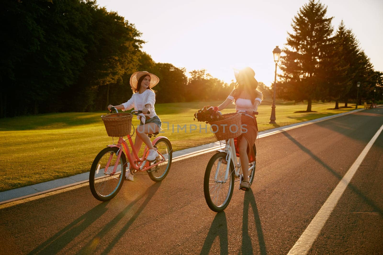 Two young females cycling together along local road at sunset. Friend relationships and happy travel at countryside