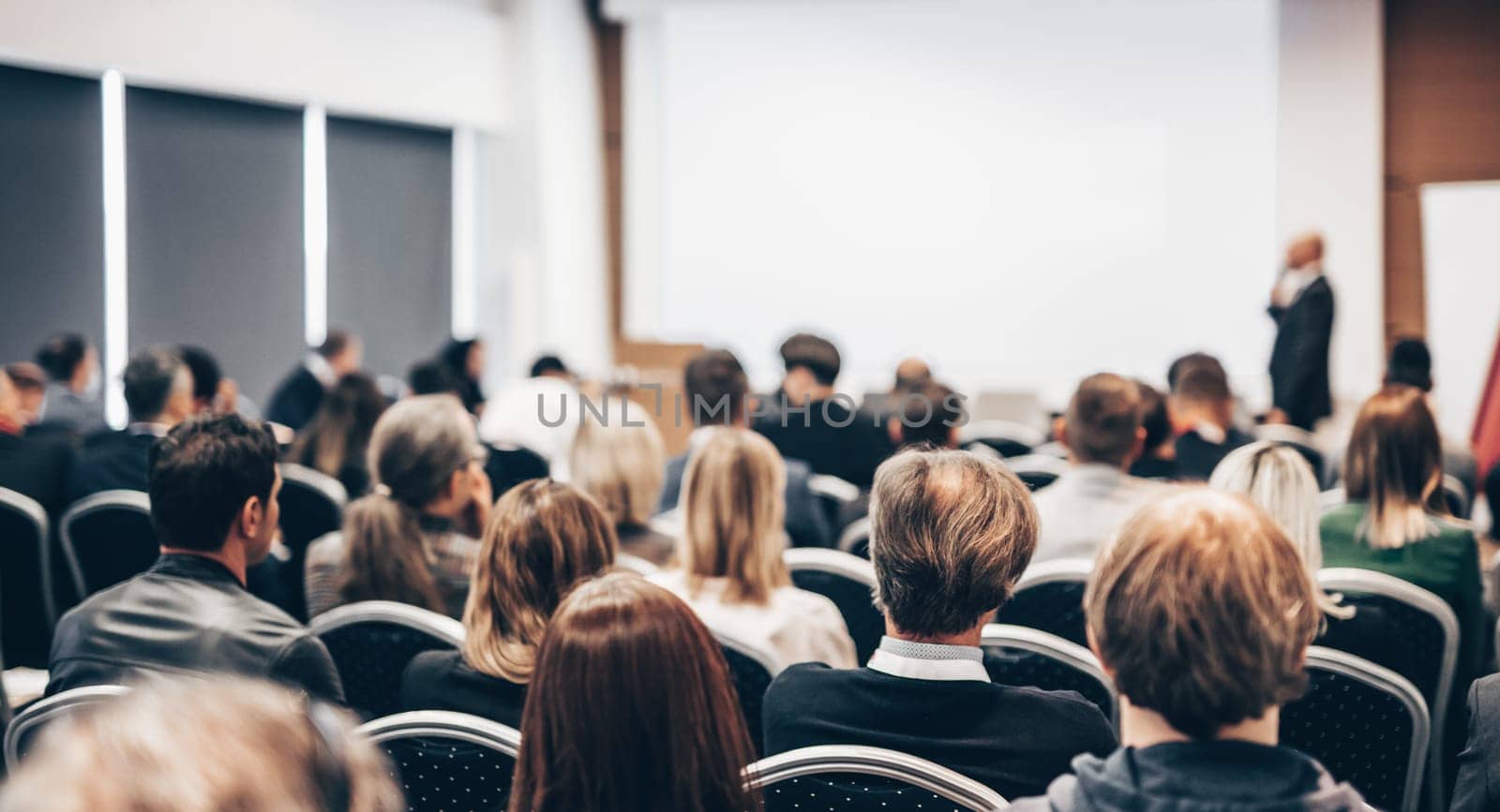 Speaker giving a talk in conference hall at business event. Rear view of unrecognizable people in audience at the conference hall. Business and entrepreneurship concept