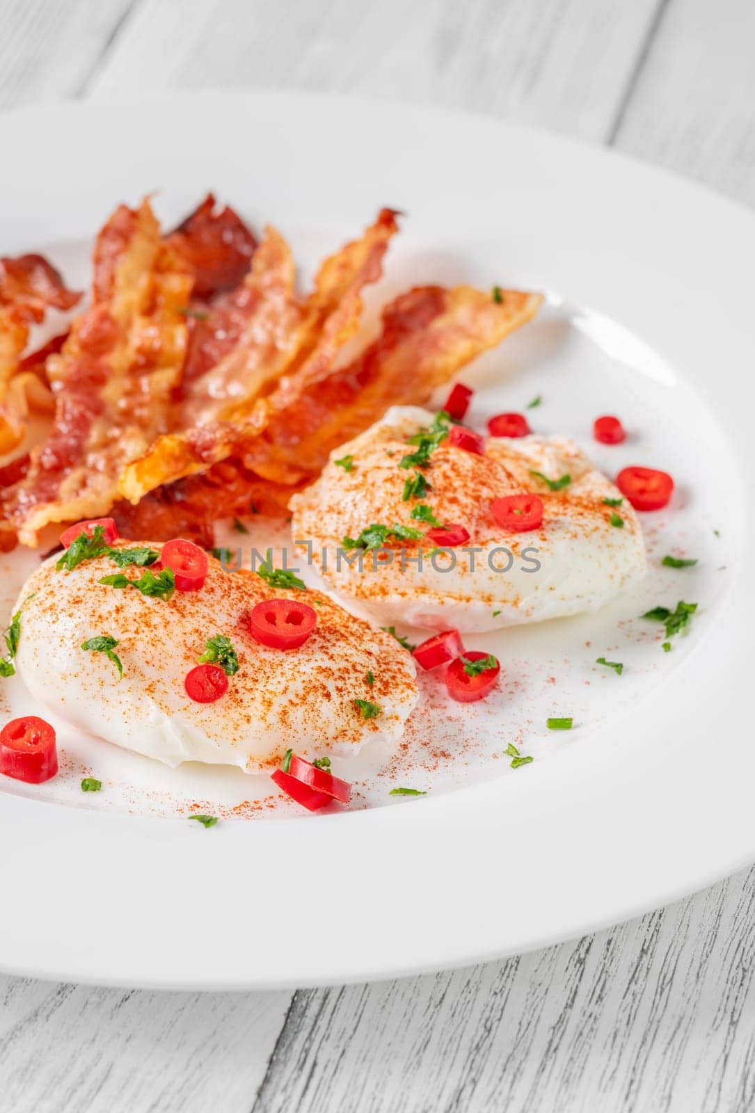 Portion of chili poached eggs with crispy bacon
