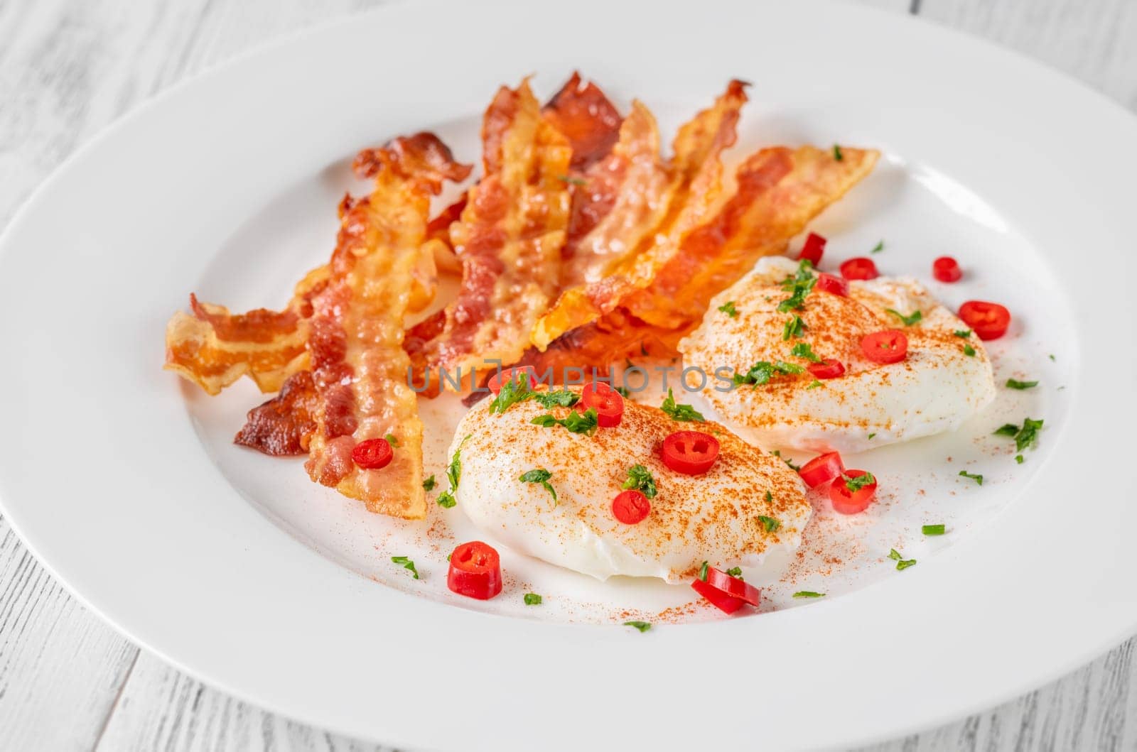 Portion of chili poached eggs with crispy bacon