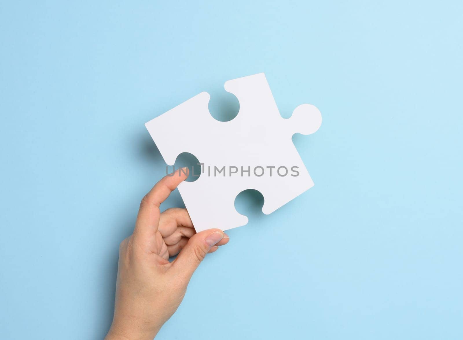 A female hand holds a white paper puzzle piece against a blue background