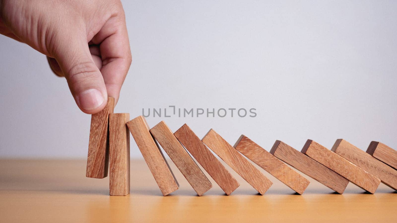 Businessman hand stopping falling blocks on table, stopping the domino effect concept for business solution, strategy and successful intervention.