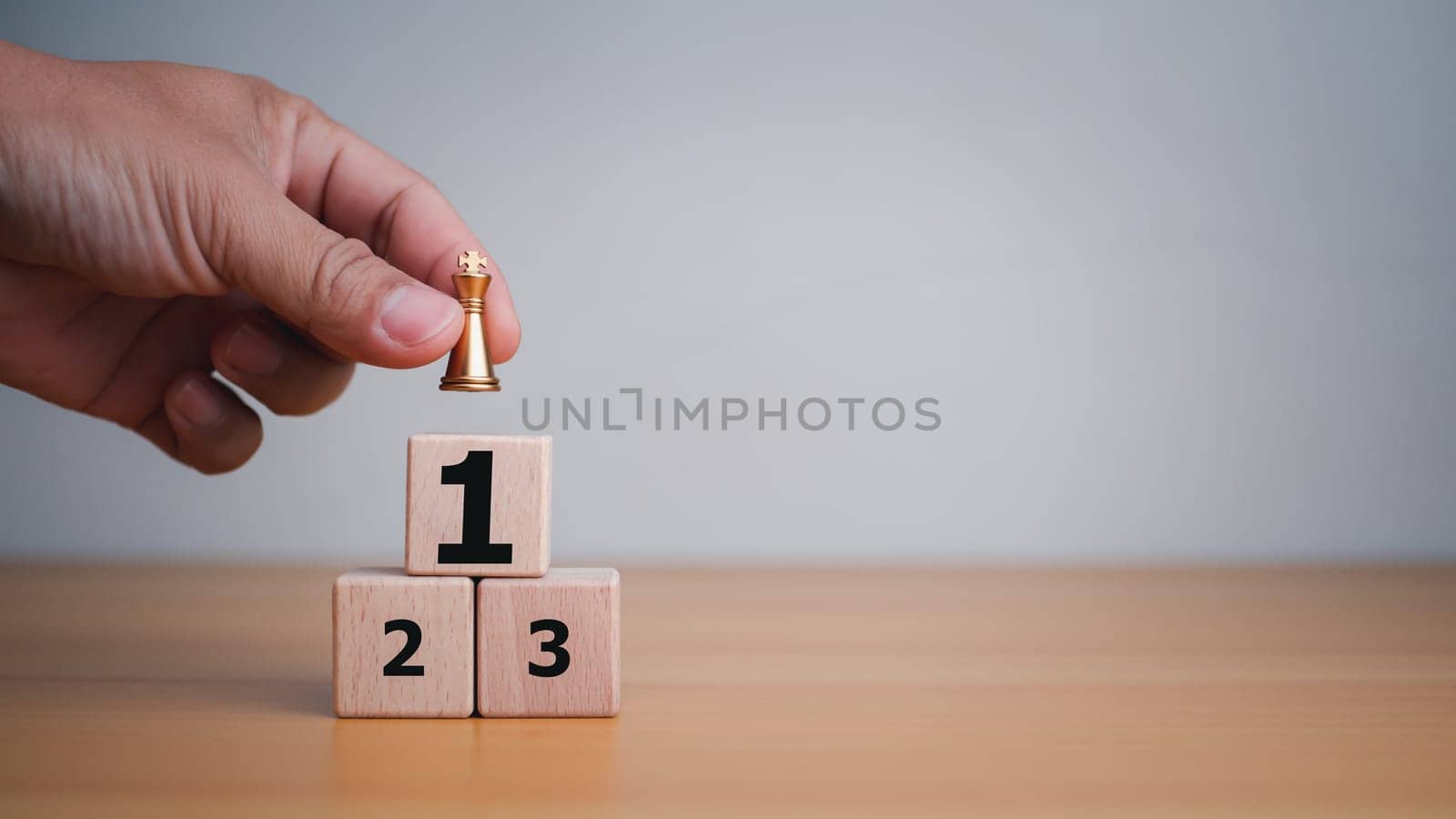 Businessman hand holding a king placed on the topmost layer of wood. It represents the concept of competition and strategic adjustments for competitors in the business.