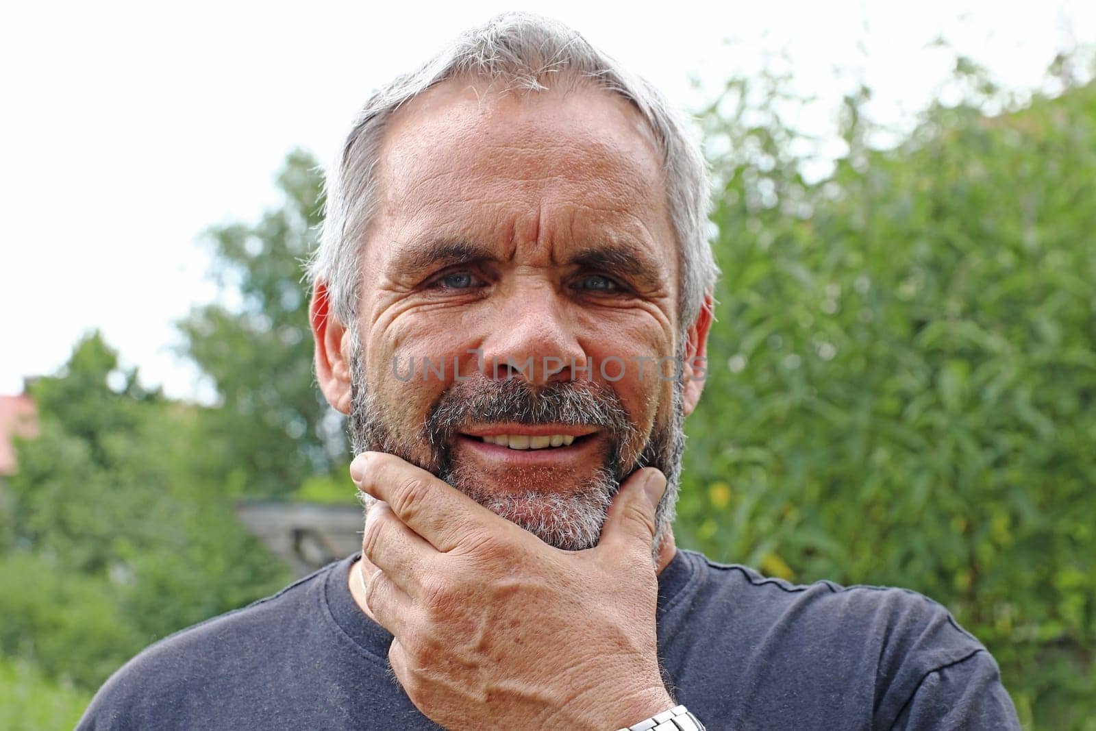 A man with gray hair and a beard laughs into the camera