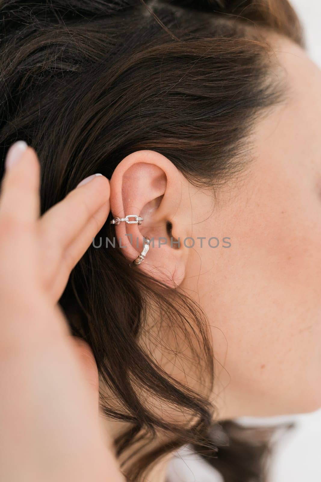 Cropped close-up shot of a young woman with asymmetrical silver ear cuffs. Female with metal ear cuffs, side view.