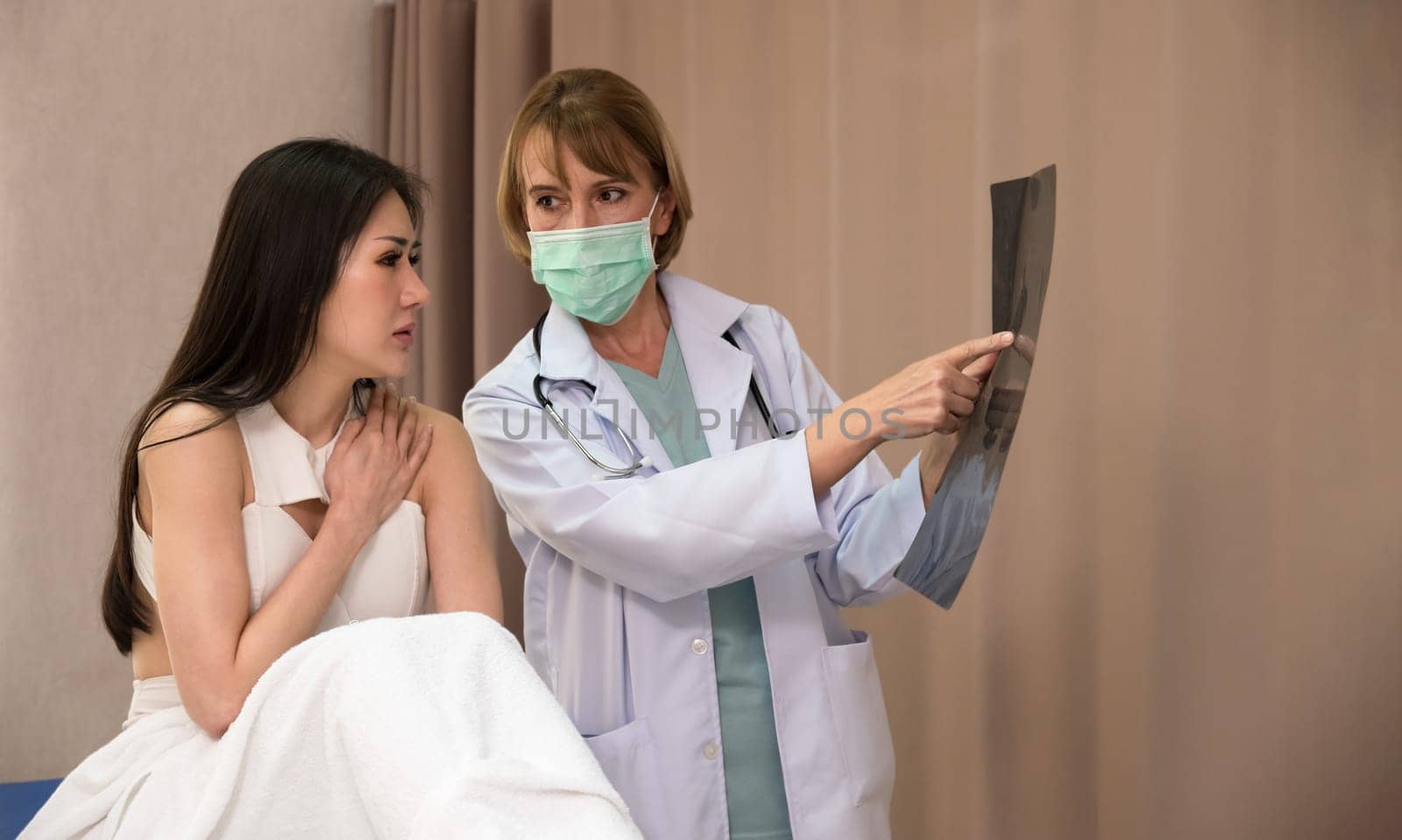 Doctor and patient discussing scan results in hospital. Female doctor checking examining x-ray film of woman patient while sitting on bed at hospital ward.