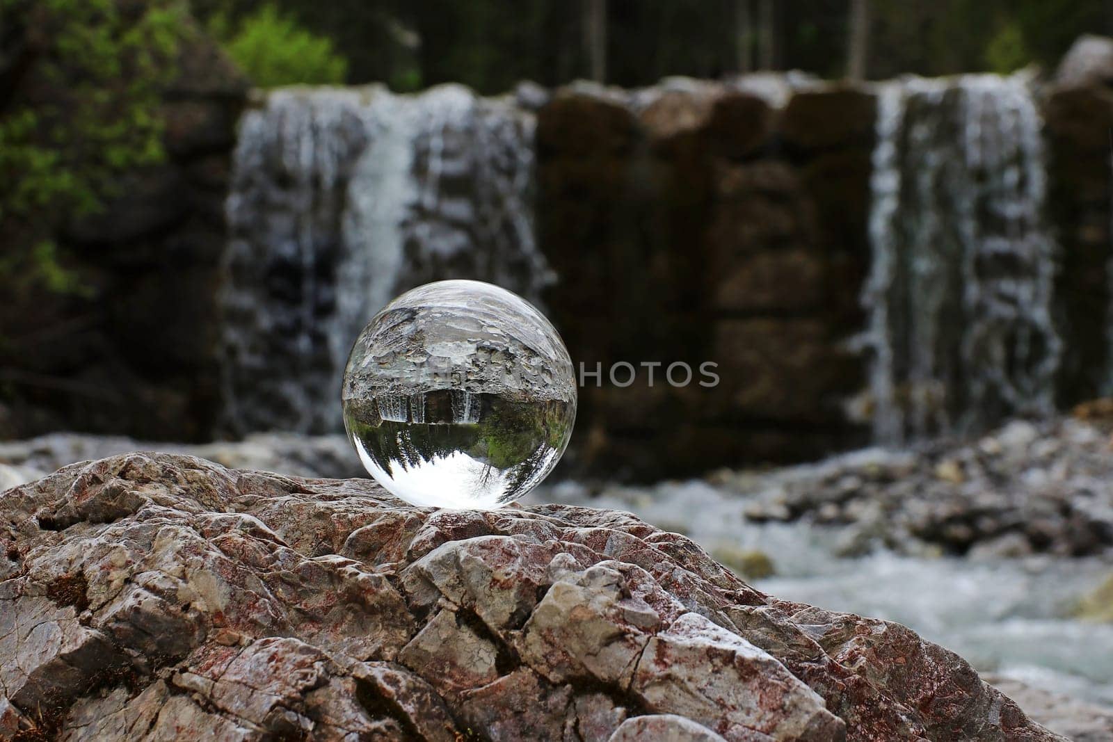 A glass sphere reflects a waterfall in the mountains