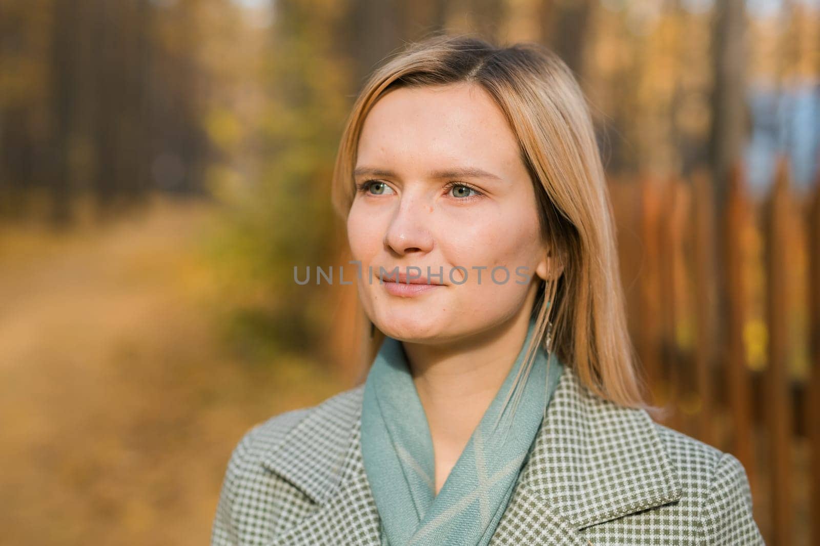 Blonde woman in elegant gray coat walks in the sunny autumn season park. Generation z and gen z youth concept