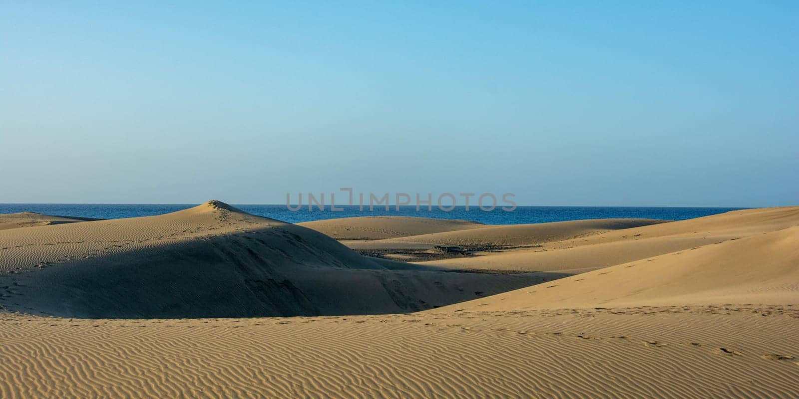 In the dunes of Maspalomas on Gran Canaria in Spain. View of the sea, with blue sky. The huge sand dunes resemble a small desert and are a nature reserve.