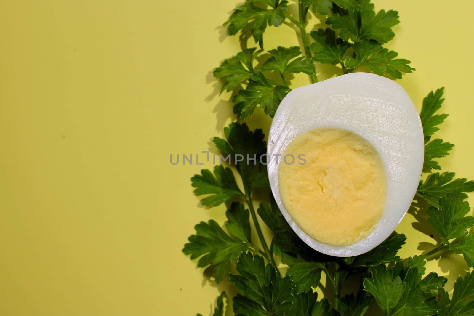 Green parsley and a boiled chicken egg on a yellow background.